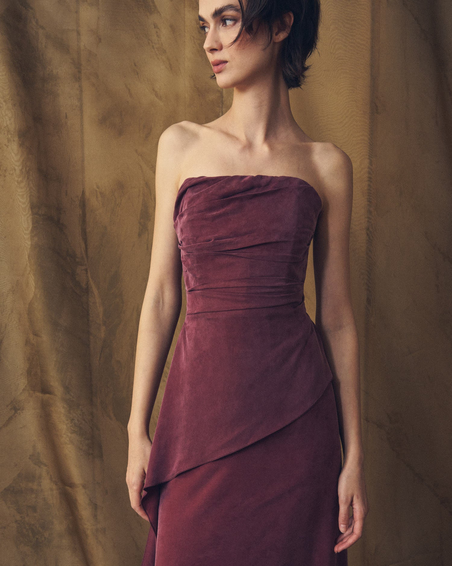 Medium shot front view of the strapless Alina cupro dress in burgundy highlighting the pleated bodice detailing by T.ba