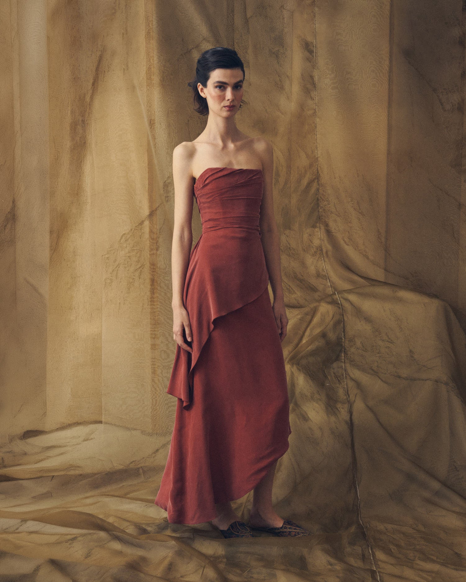 Full-length front studio view of model wearing the strapless Alina long cupro dress in copper with asymmetrical draping by T.ba