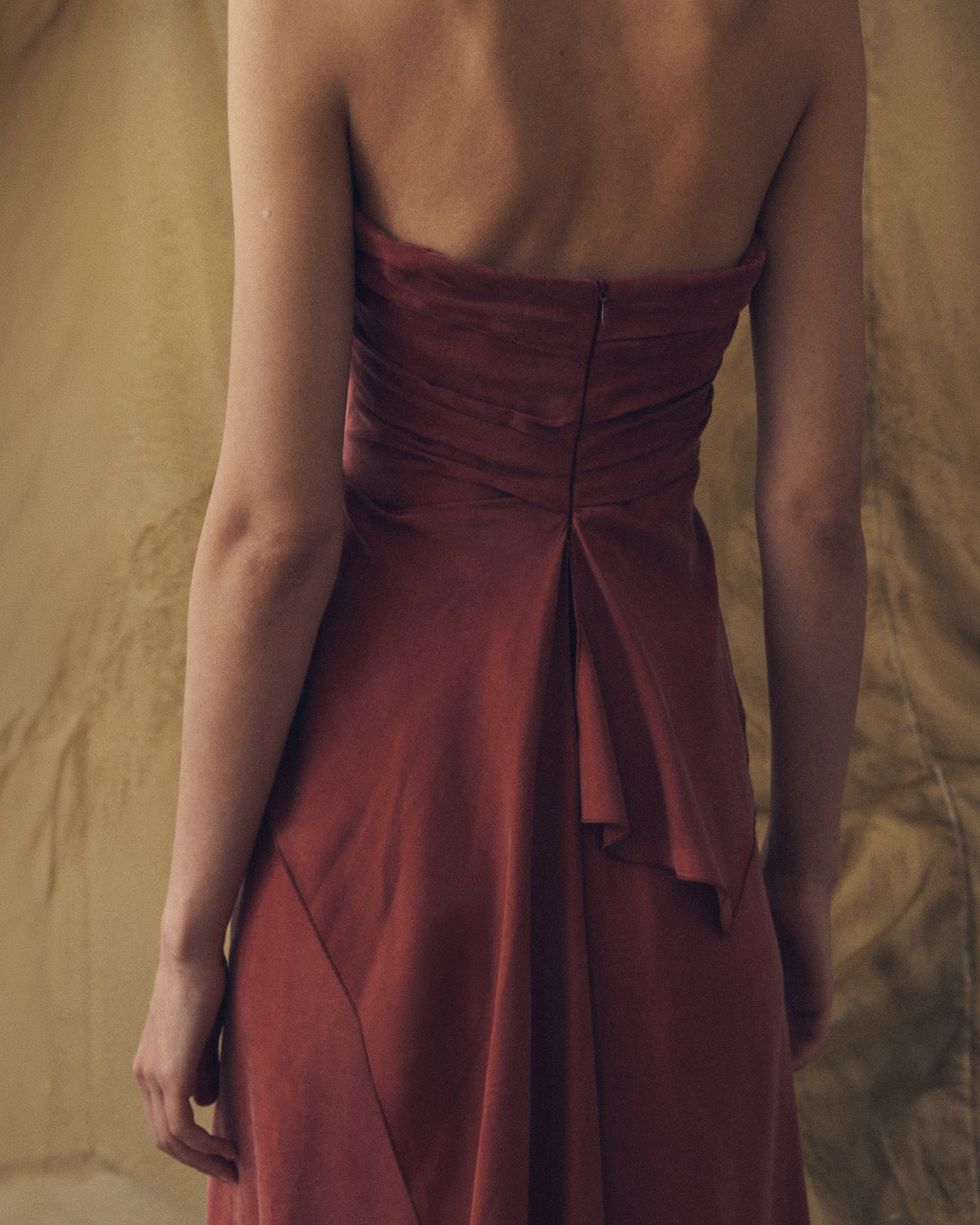 Close-up back view showing the open back and draped fabric detail of the Alina long cupro dress in copper by T.ba