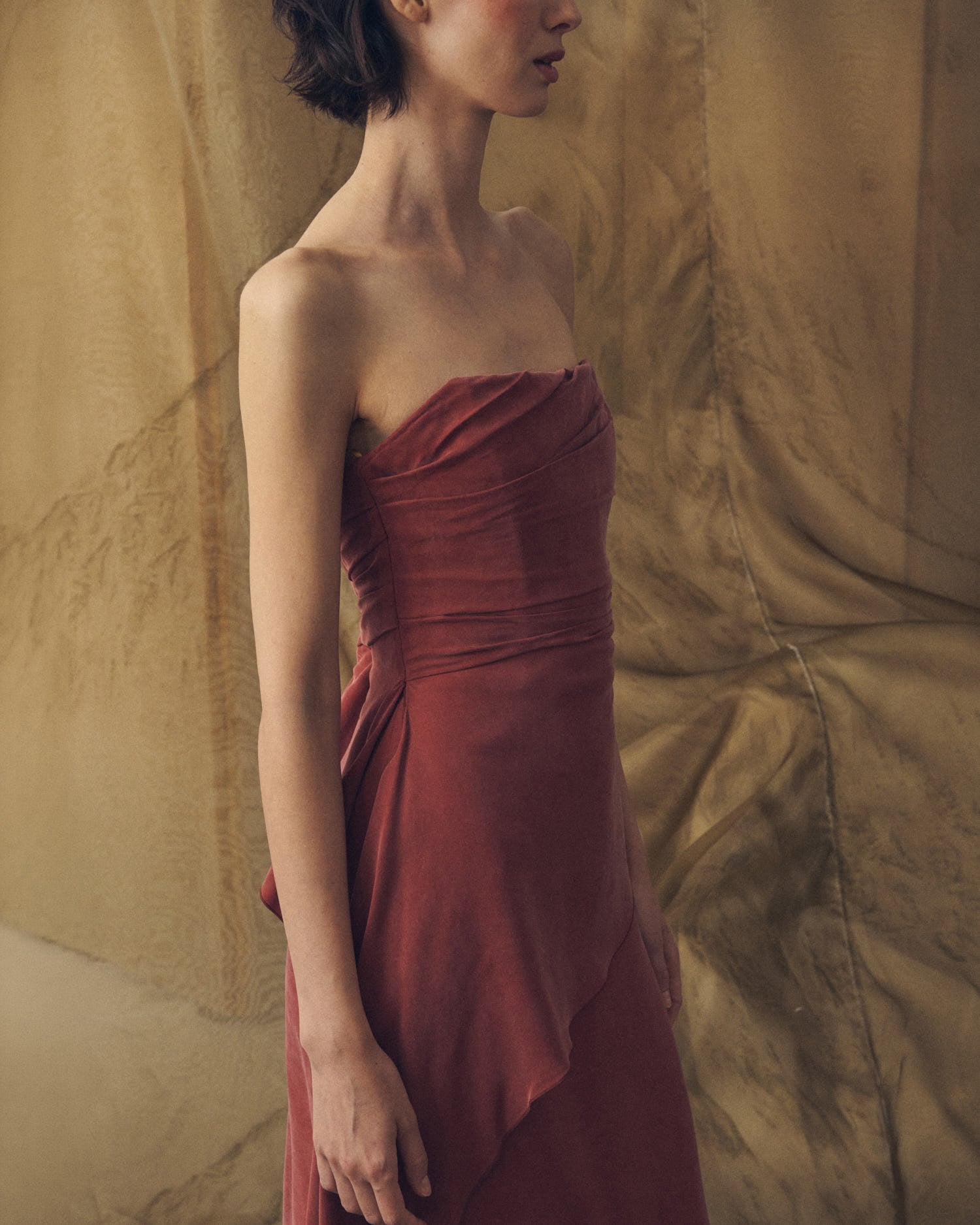Upper body three-quarter studio view of model wearing the strapless Alina long cupro dress in copper by T.ba