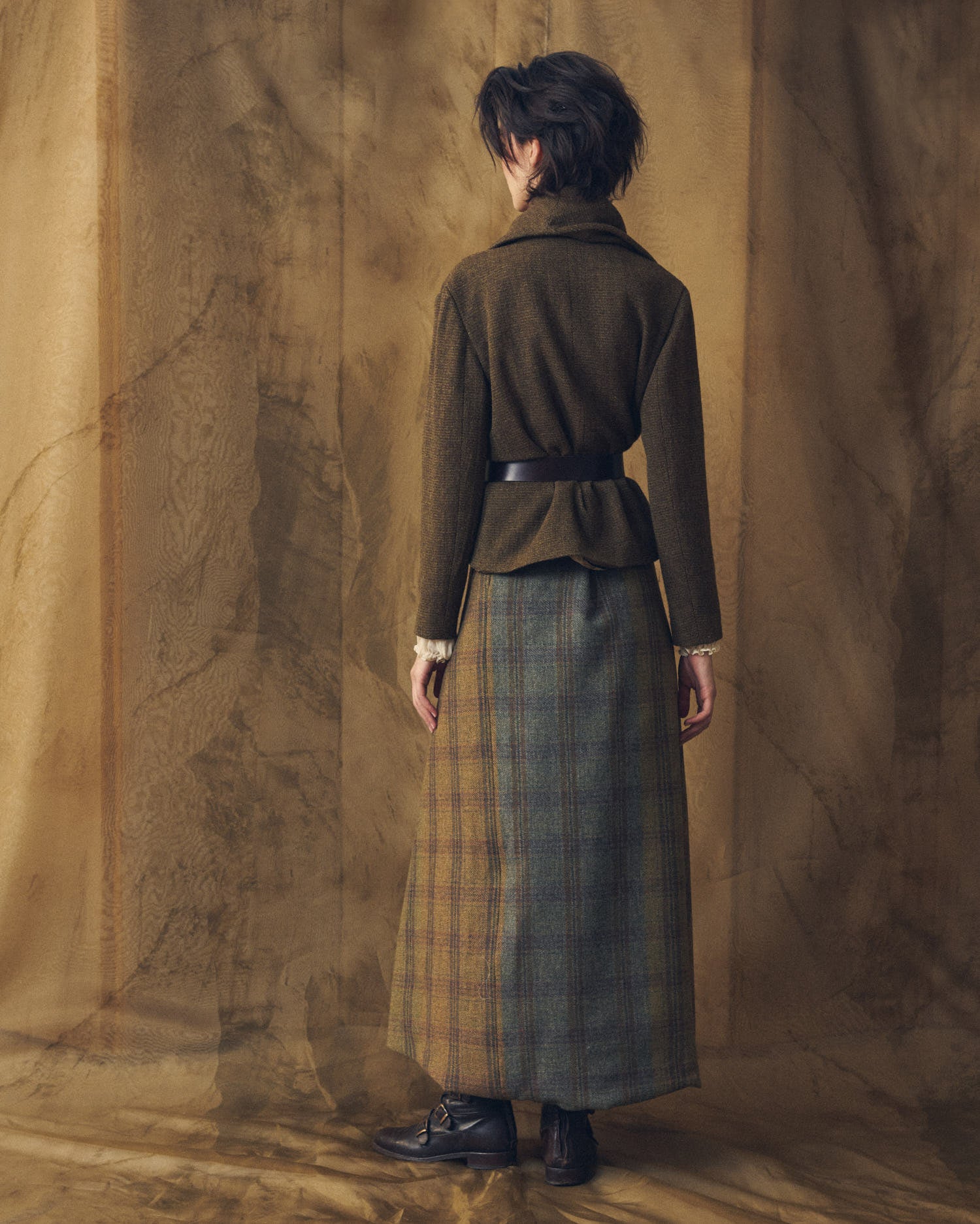 Back view of model wearing the Alina Tweed short brown wool jacket structured with a leather belt by T.ba