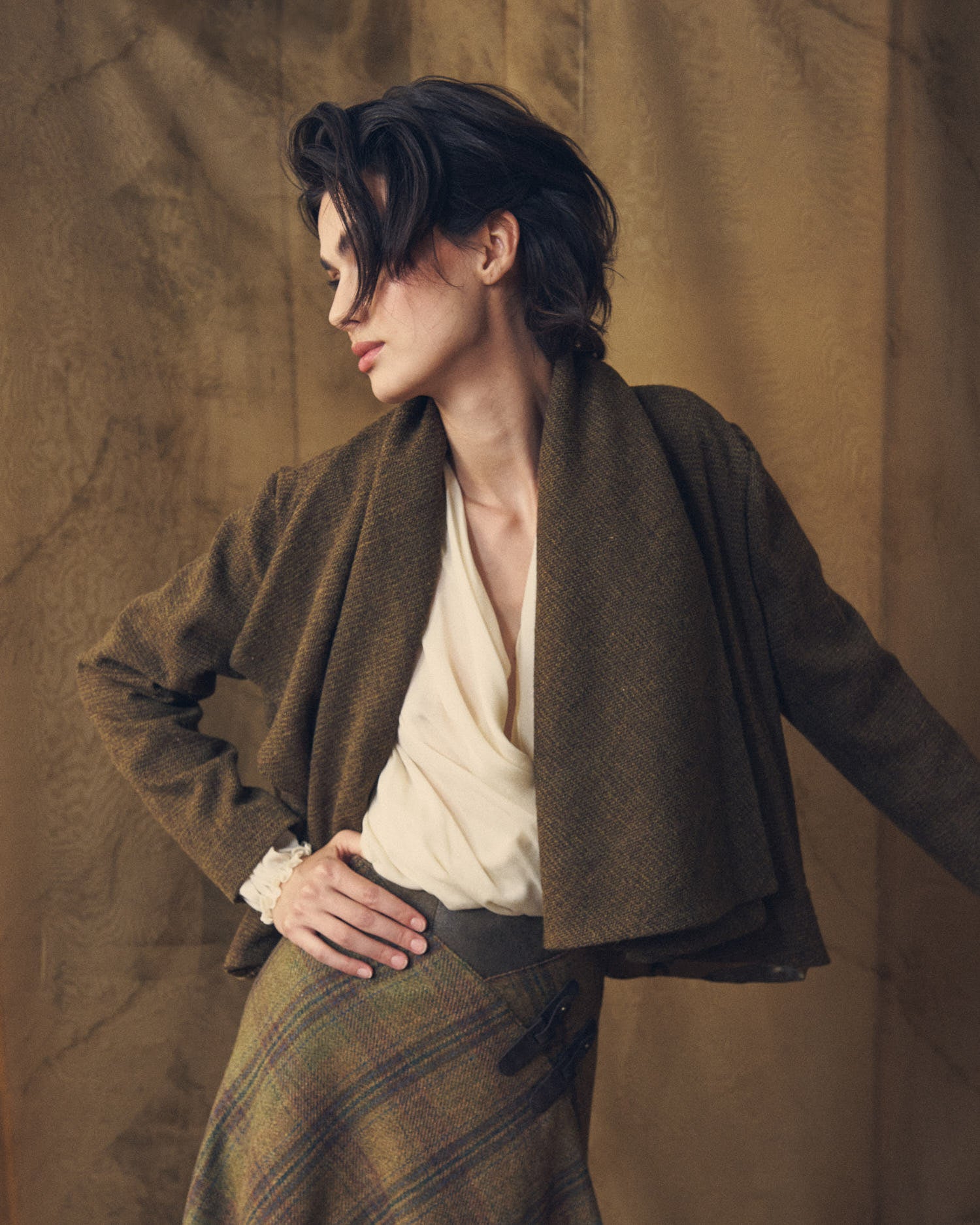 Model posing in the open Alina Tweed short jacket with draped front panels in brown wool by T.ba