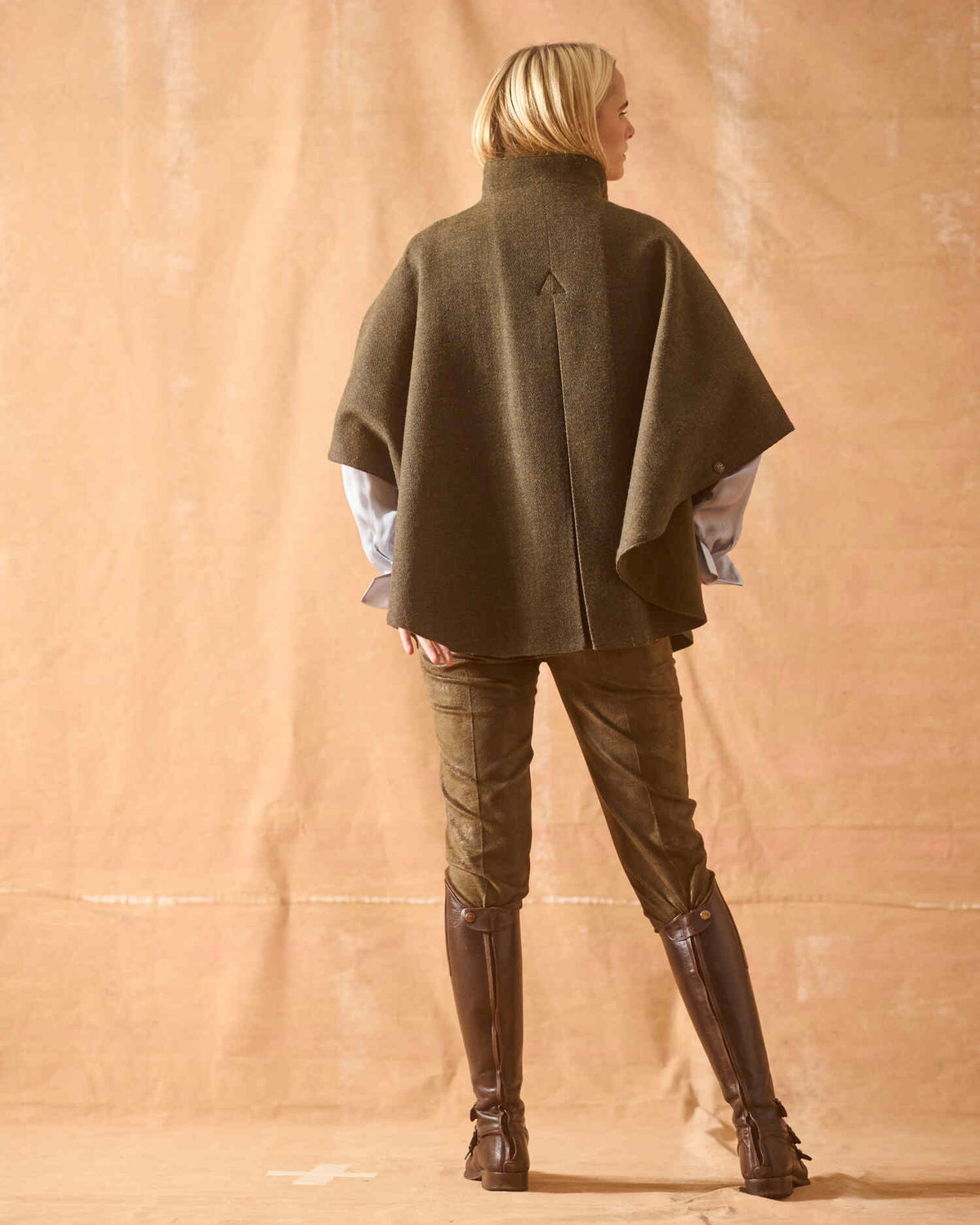 Back view of model wearing dark chocolate leather knee-high boots with back zippers and cape coat T.ba