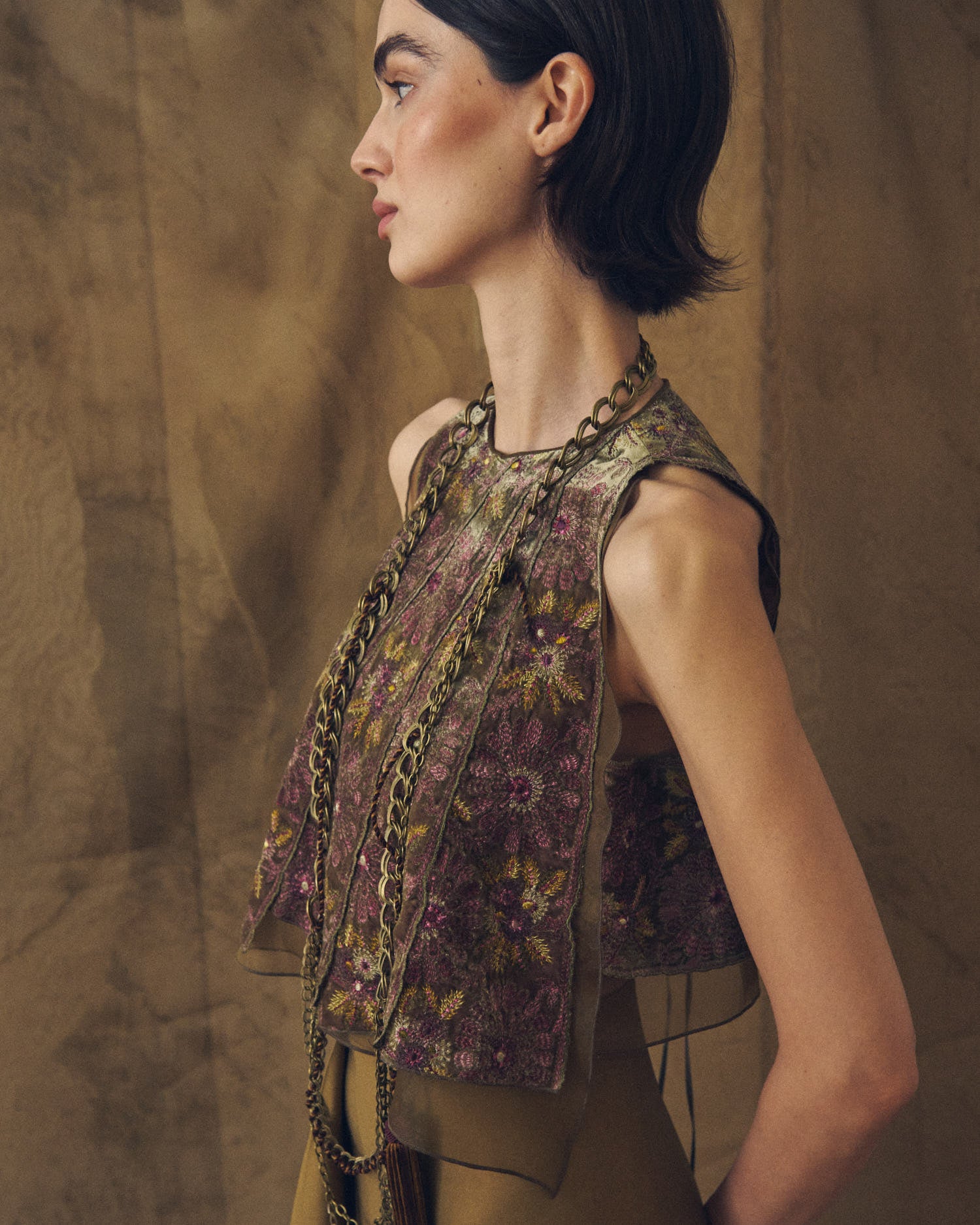 Side profile studio shot of model wearing the Baltea Borgogna gold link chain belt styled around the neck over an embroidered top by T.ba