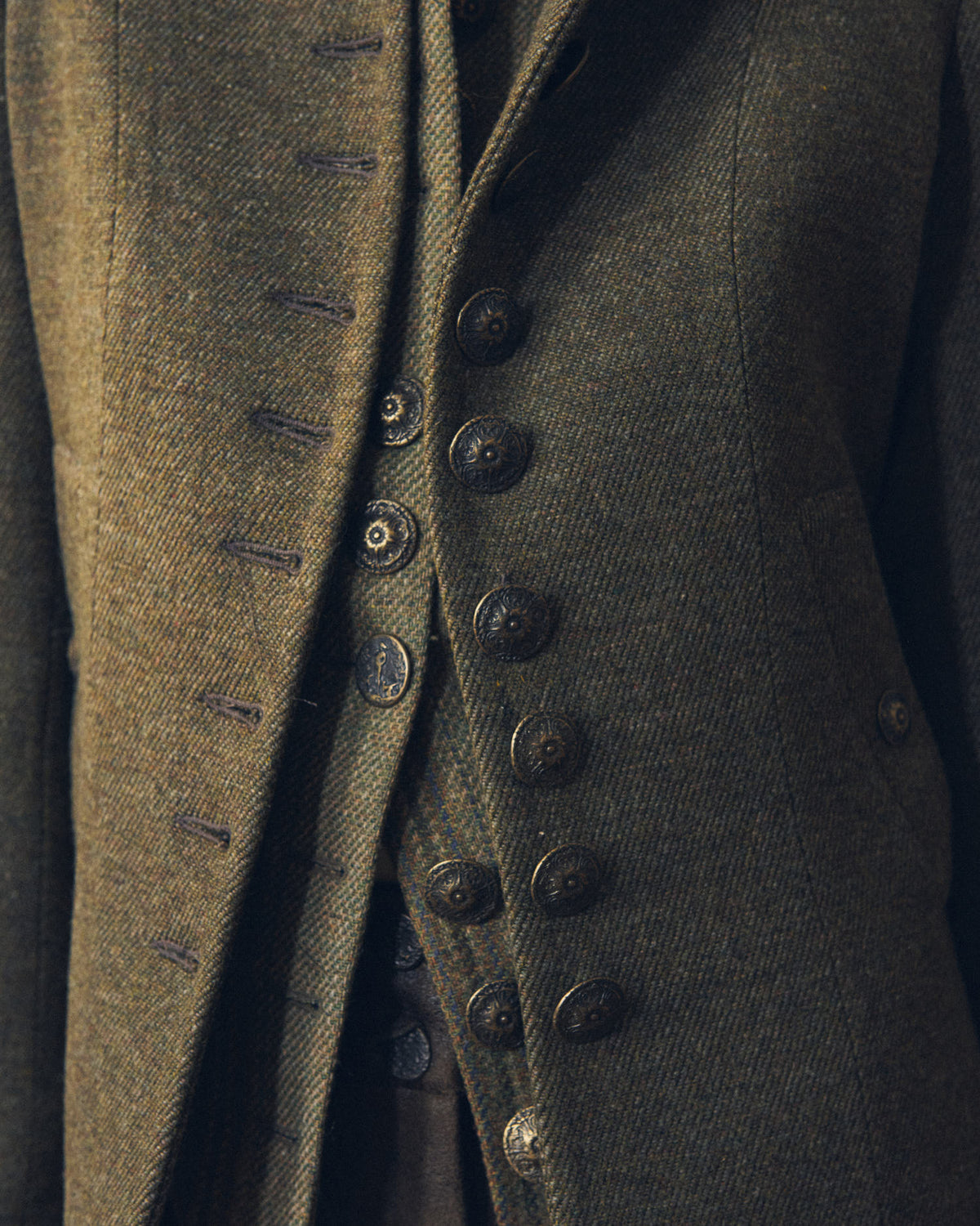 Close-up view of the front placket and embossed metal buttons on the Baltea Tweed jacket by T.ba