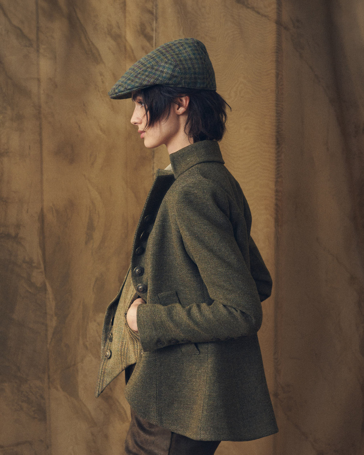 Profile view of model wearing the Baltea Tweed jacket in brown green wool with flat cap by T.ba