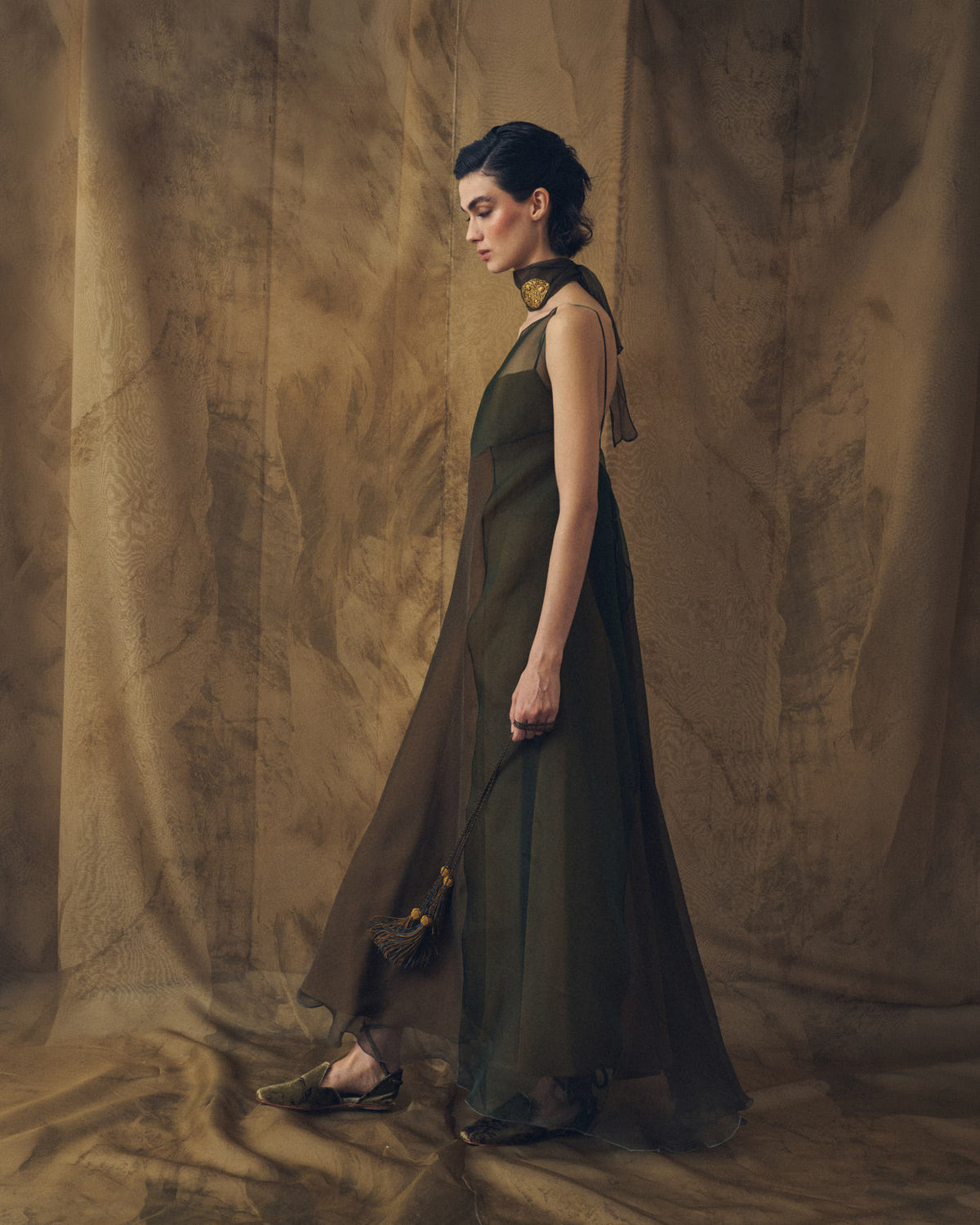 Full-length side profile view of model wearing the Biella fluid organza maxi dress in hunting green and arbequina by T.ba