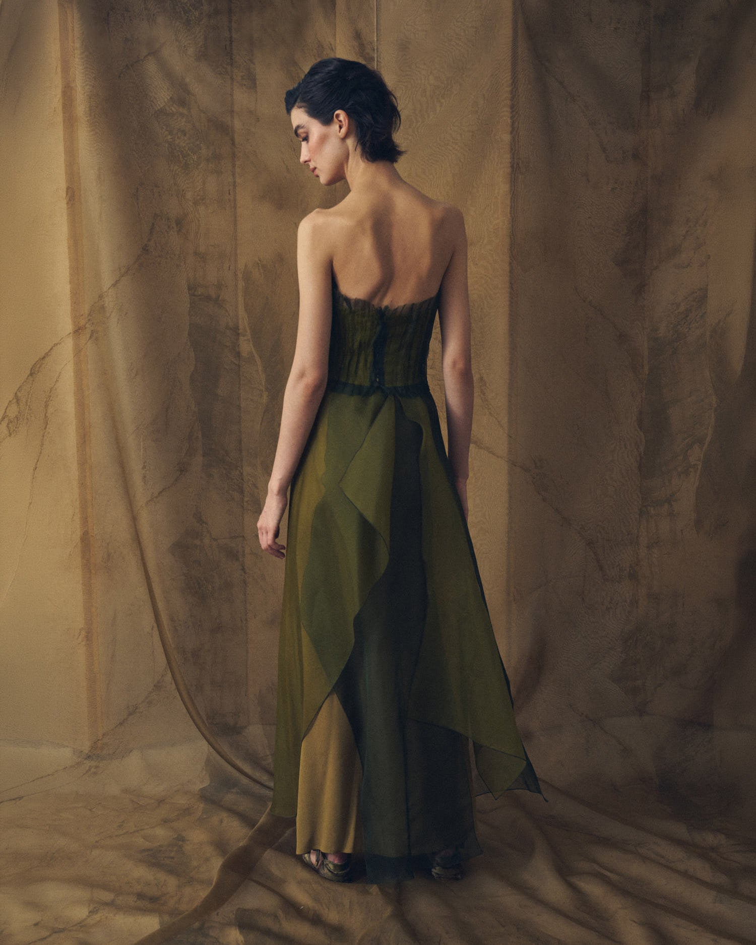 Full-length back studio view of model wearing the strapless Birdie top in hunting green showing layered sheer drape by T.ba