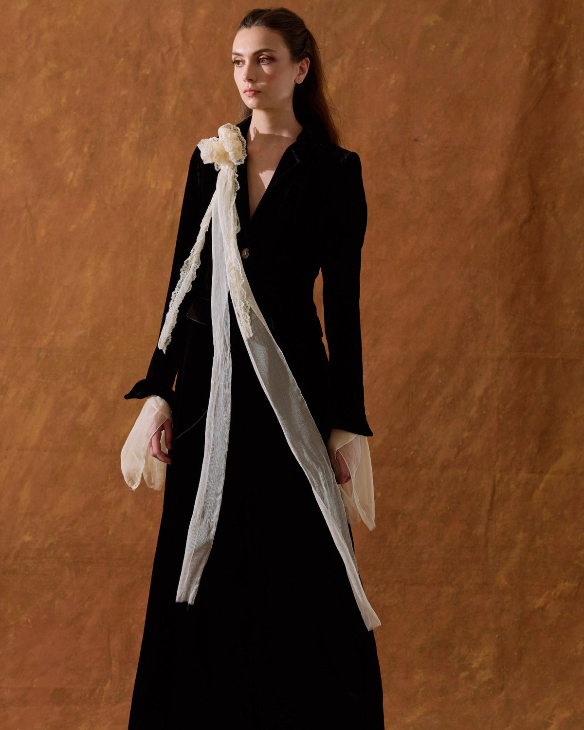 Three-quarter front view of model showcasing the fitted Classic Coat in black silk velvet styled over a long dress for women by T.ba