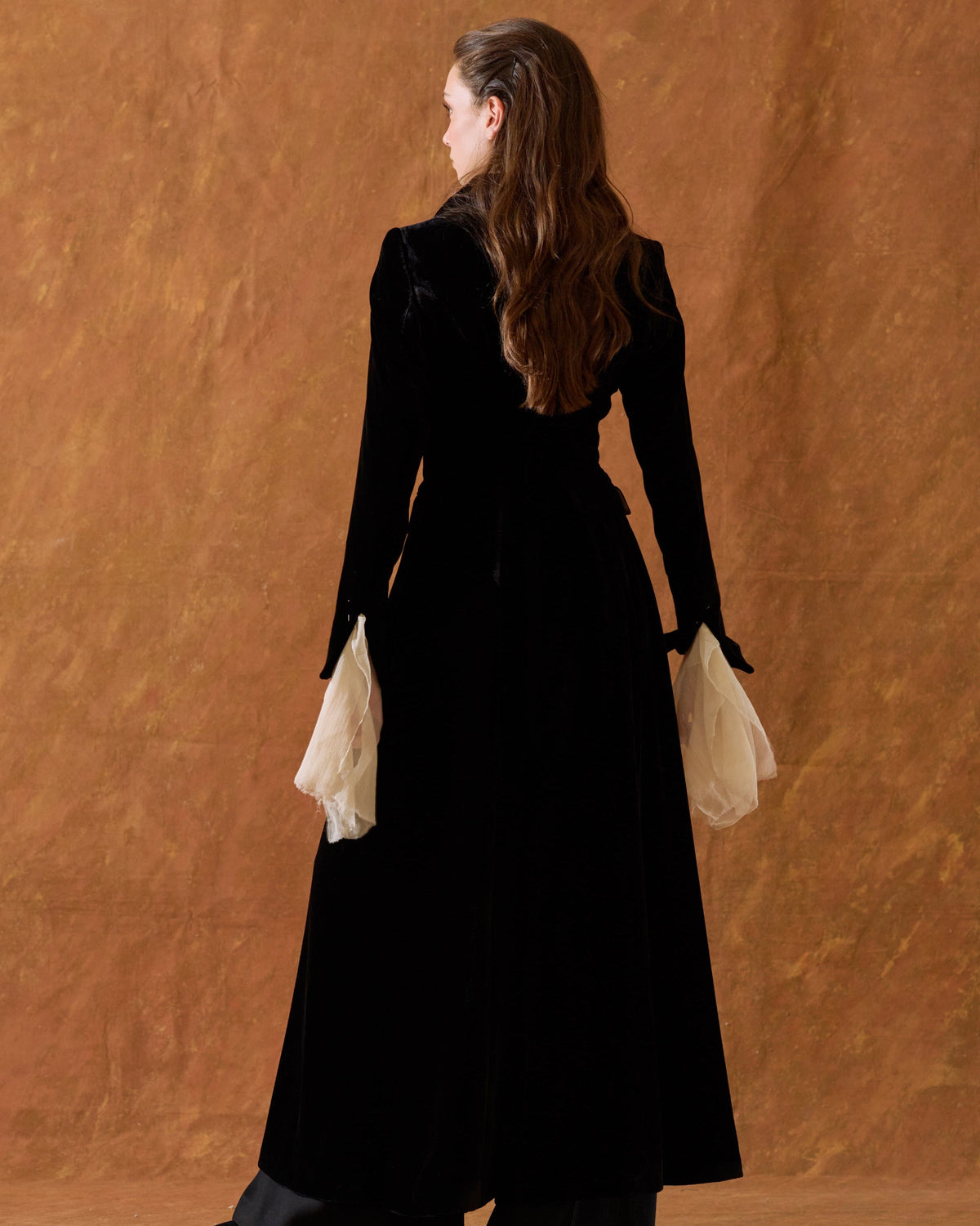 Back view of model wearing the long black silk velvet Classic Coat showing the structured waist and contrasting flared cuffs for women by T.ba