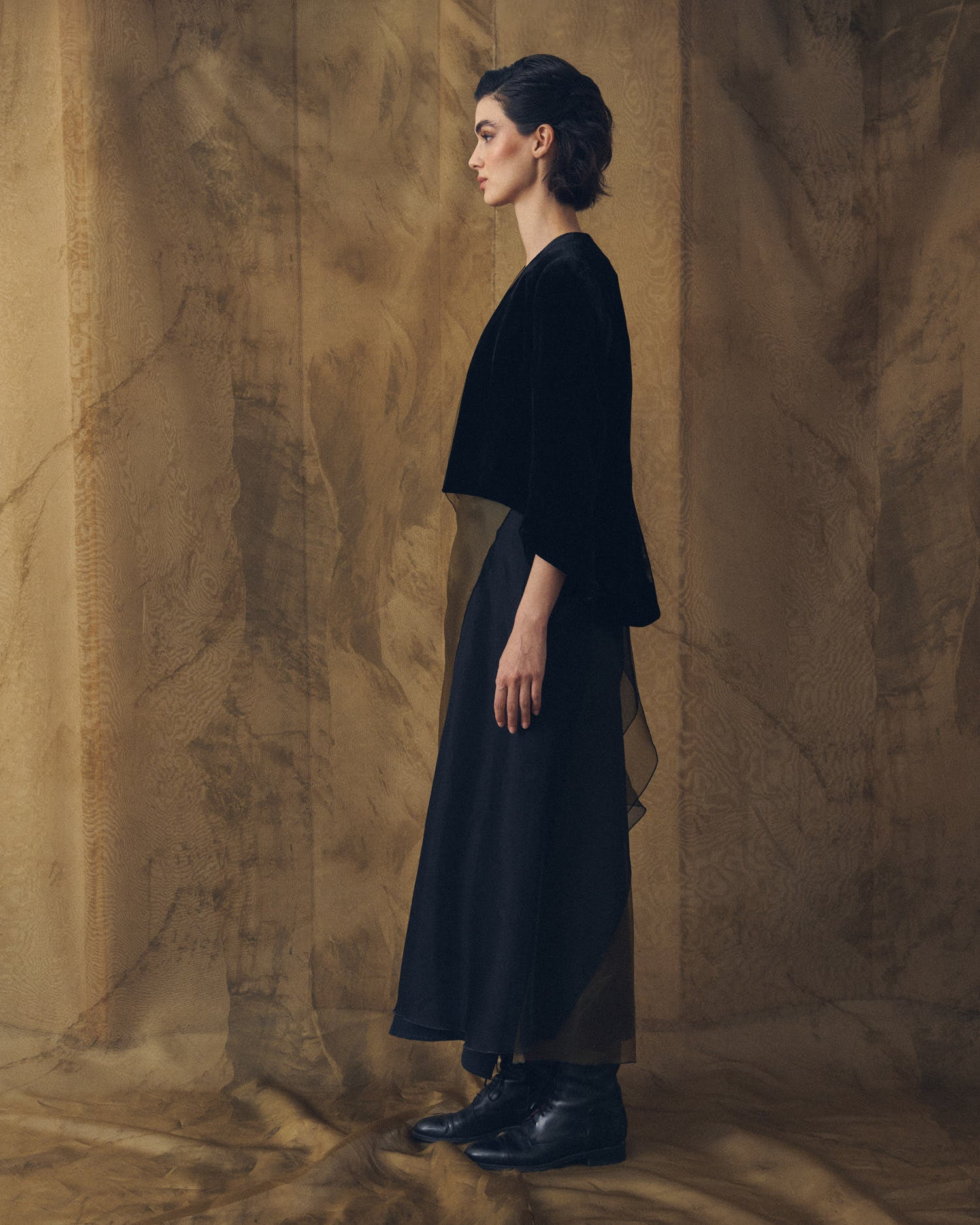 Side profile view of model wearing the cropped Daria jacket in black silk velvet by T.ba