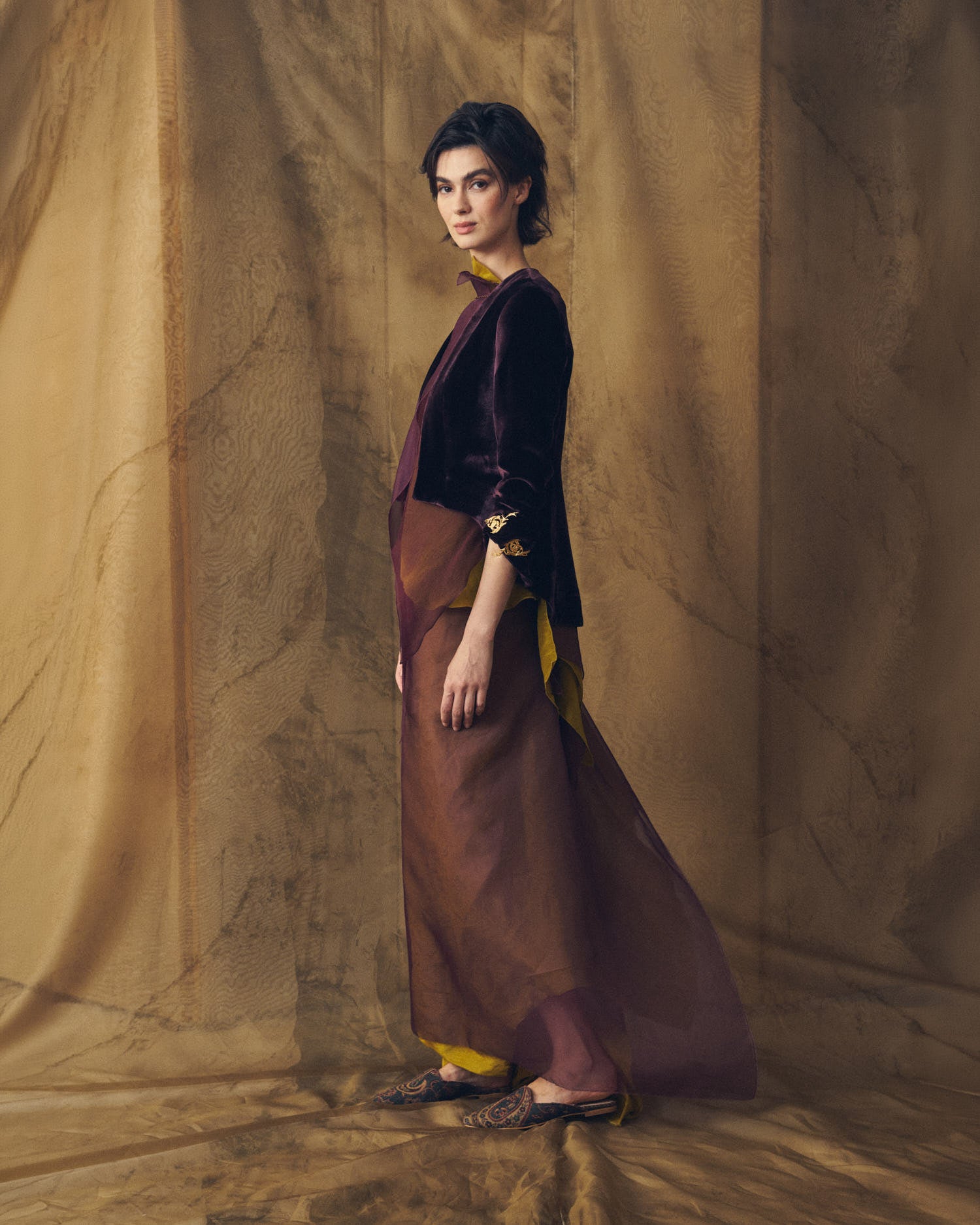Three-quarter profile view of model wearing the Daria cropped jacket in grape silk velvet by T.ba