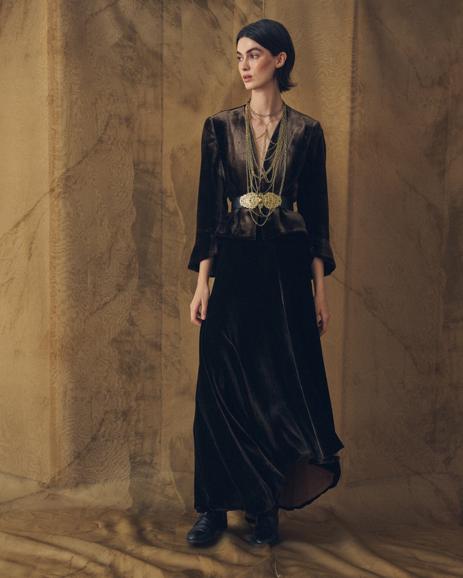Full-length view of model wearing the Daria jacket in truffle silk velvet styled with an ornate waist belt by T.ba