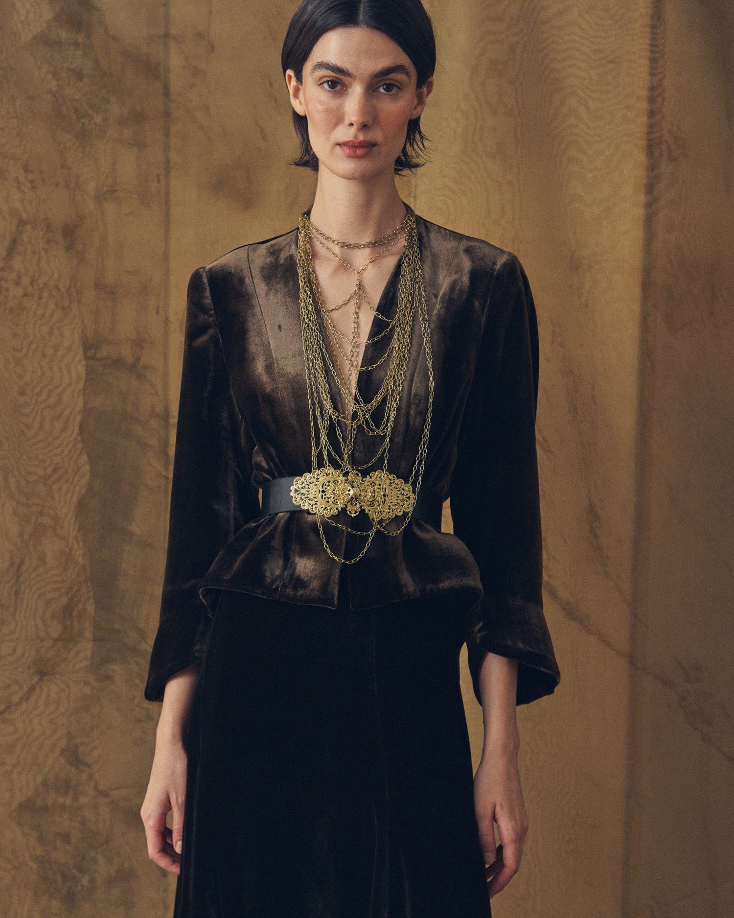Medium shot of model wearing the V-neck Daria jacket in truffle silk velvet with statement belt by T.ba