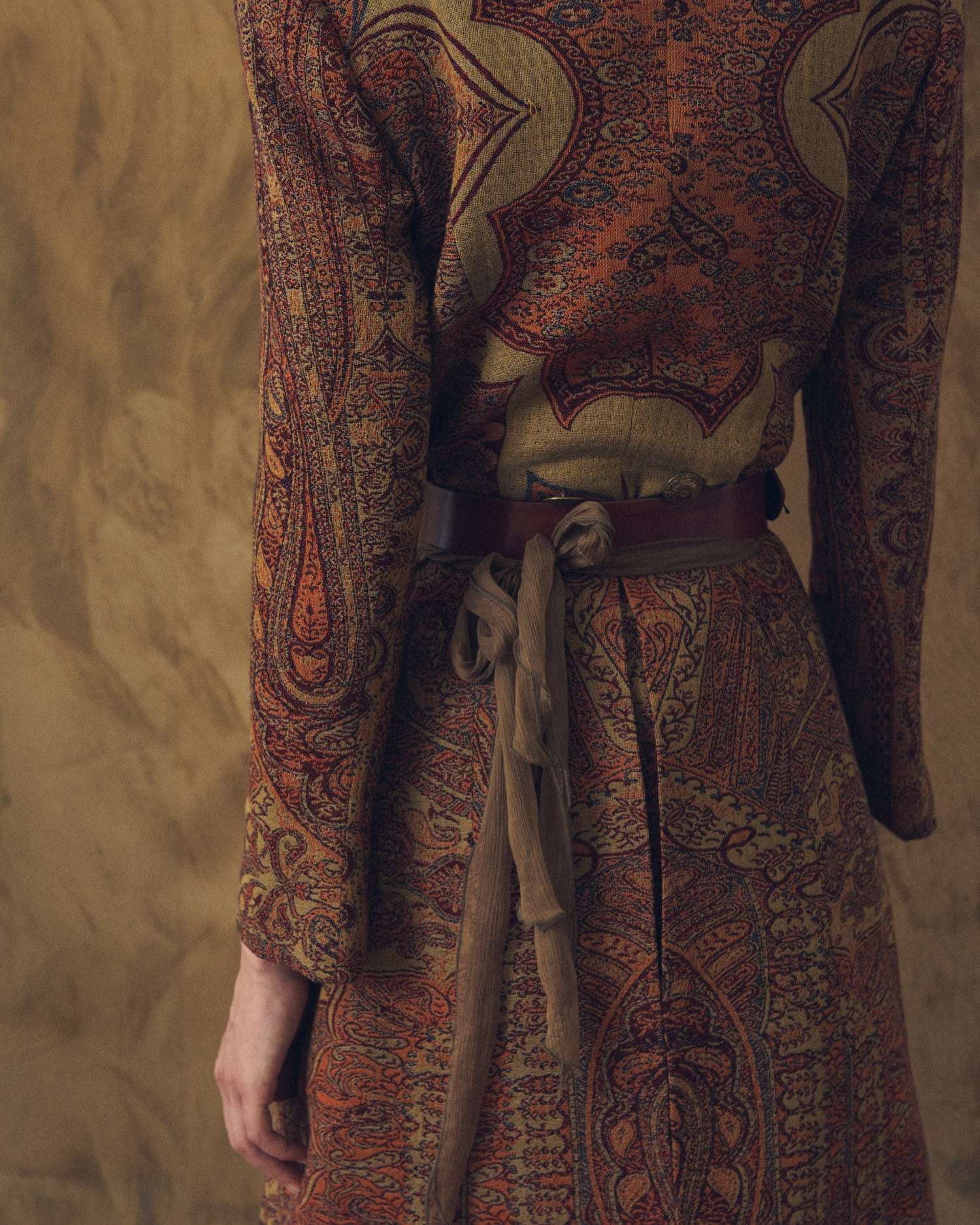 Back close-up shot of the Duke Belt khaki leather belt wrapped around the waist over a paisley weave jacket for women by T.ba
