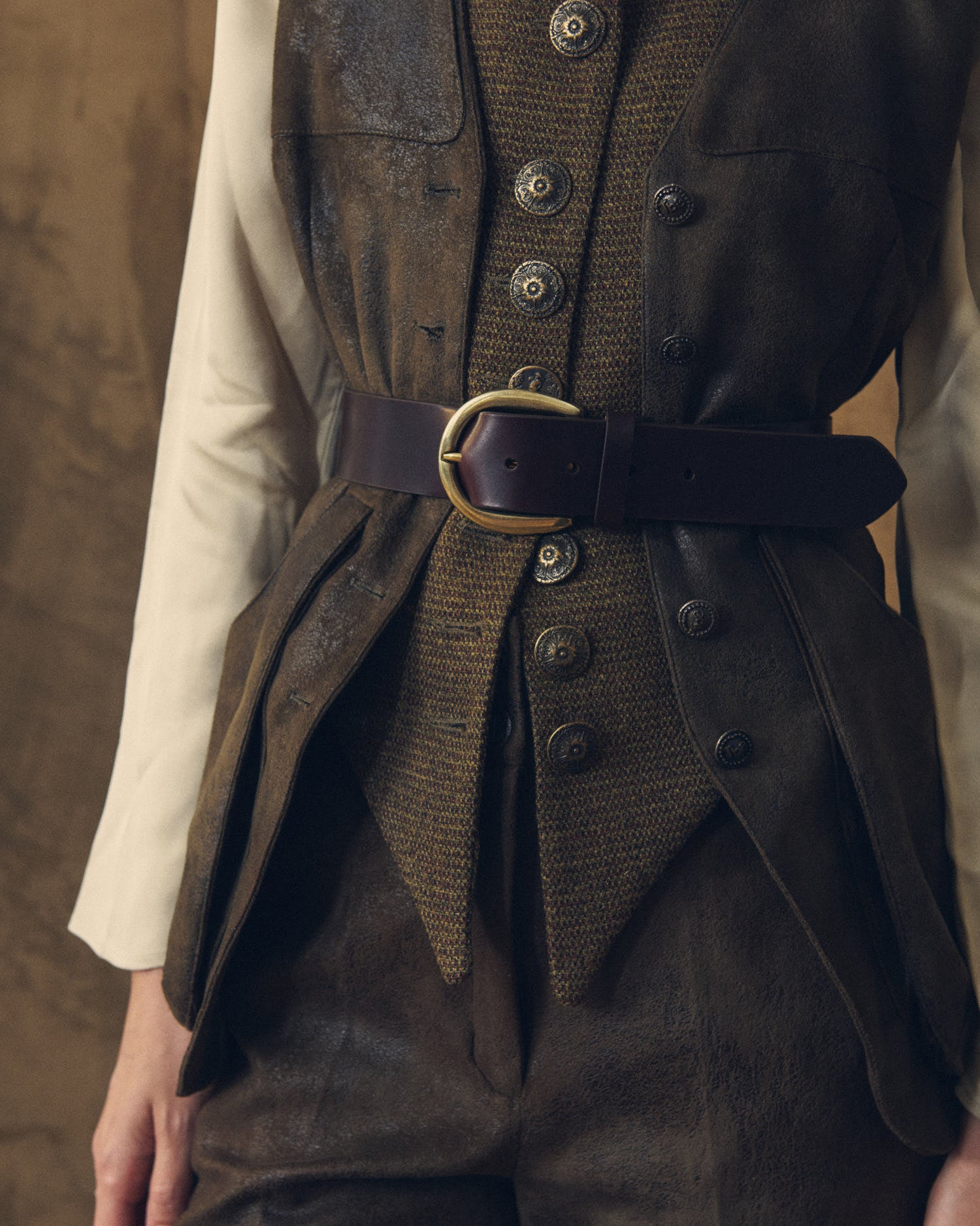 Medium close-up view of the Duke Belt wide chocolate leather belt with gold brass buckle styled over a waistcoat for women by T.ba