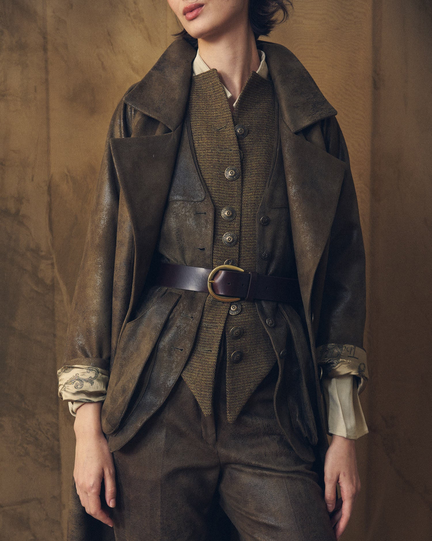 Front torso shot highlighting the Duke Belt dark chocolate leather belt with oval buckle over layered vest and coat by T.ba
