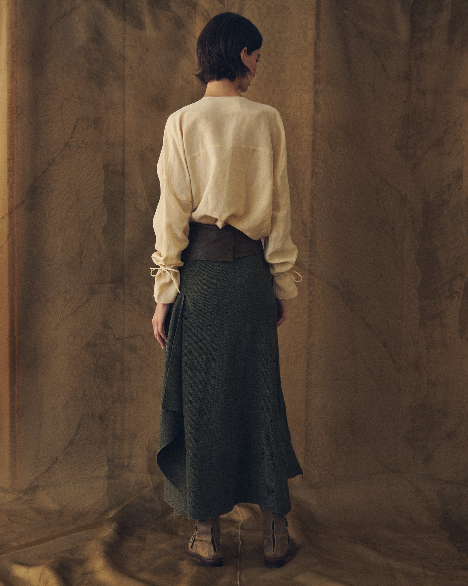Full-length back view of the natural cream Eloise Cupro Blouse styled with a high-waisted olive green skirt for women T.ba