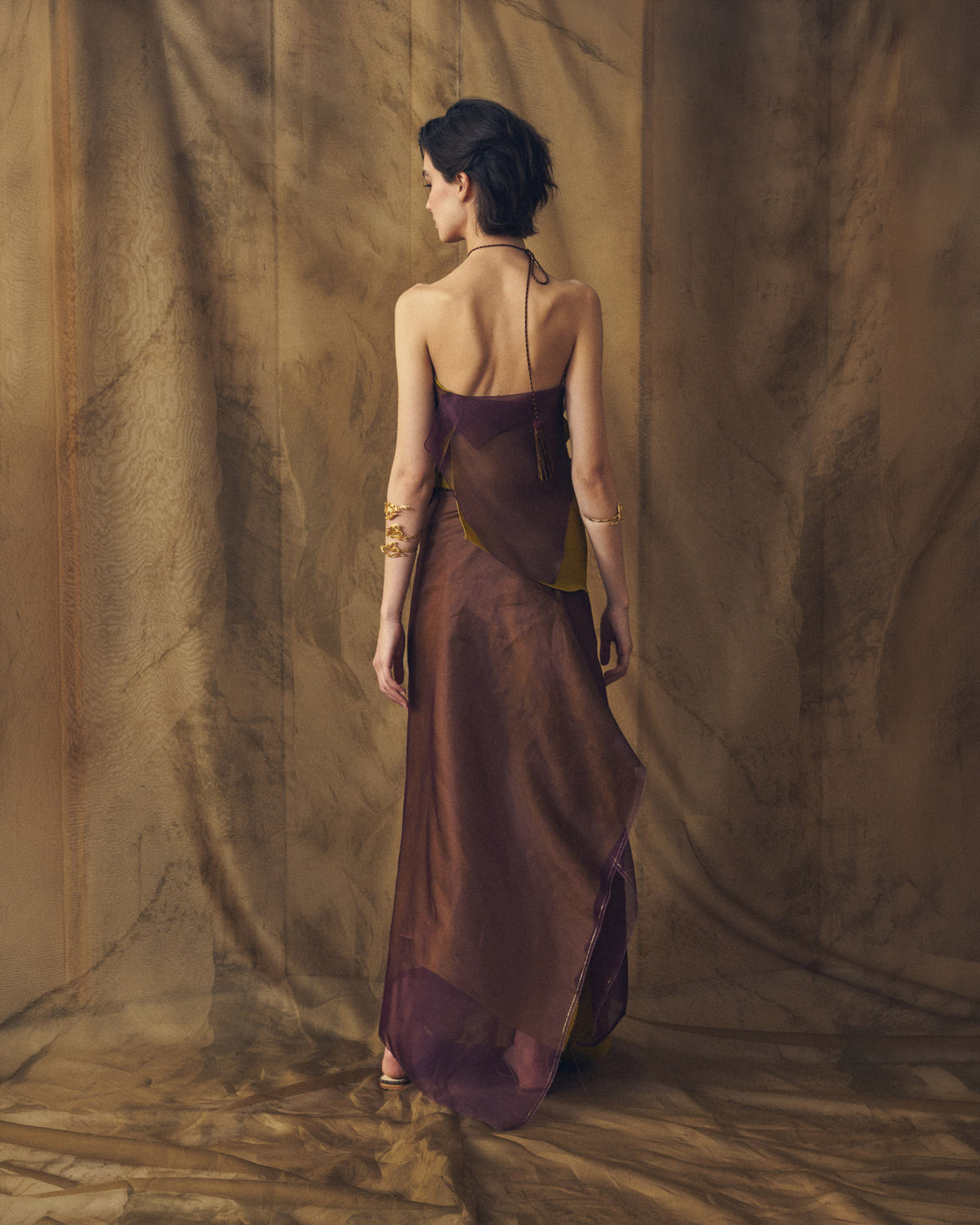 Full-length back studio view of model wearing the backless Fiore aubergine organza top with hanging tassel detail by T.ba