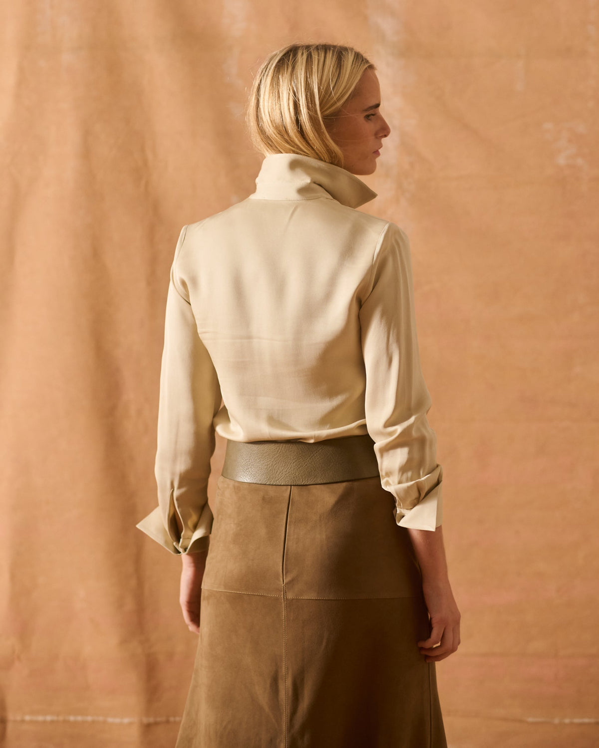 Back view of woman wearing elegant beige Sharkskin Rania silk shirt with high collar T.ba