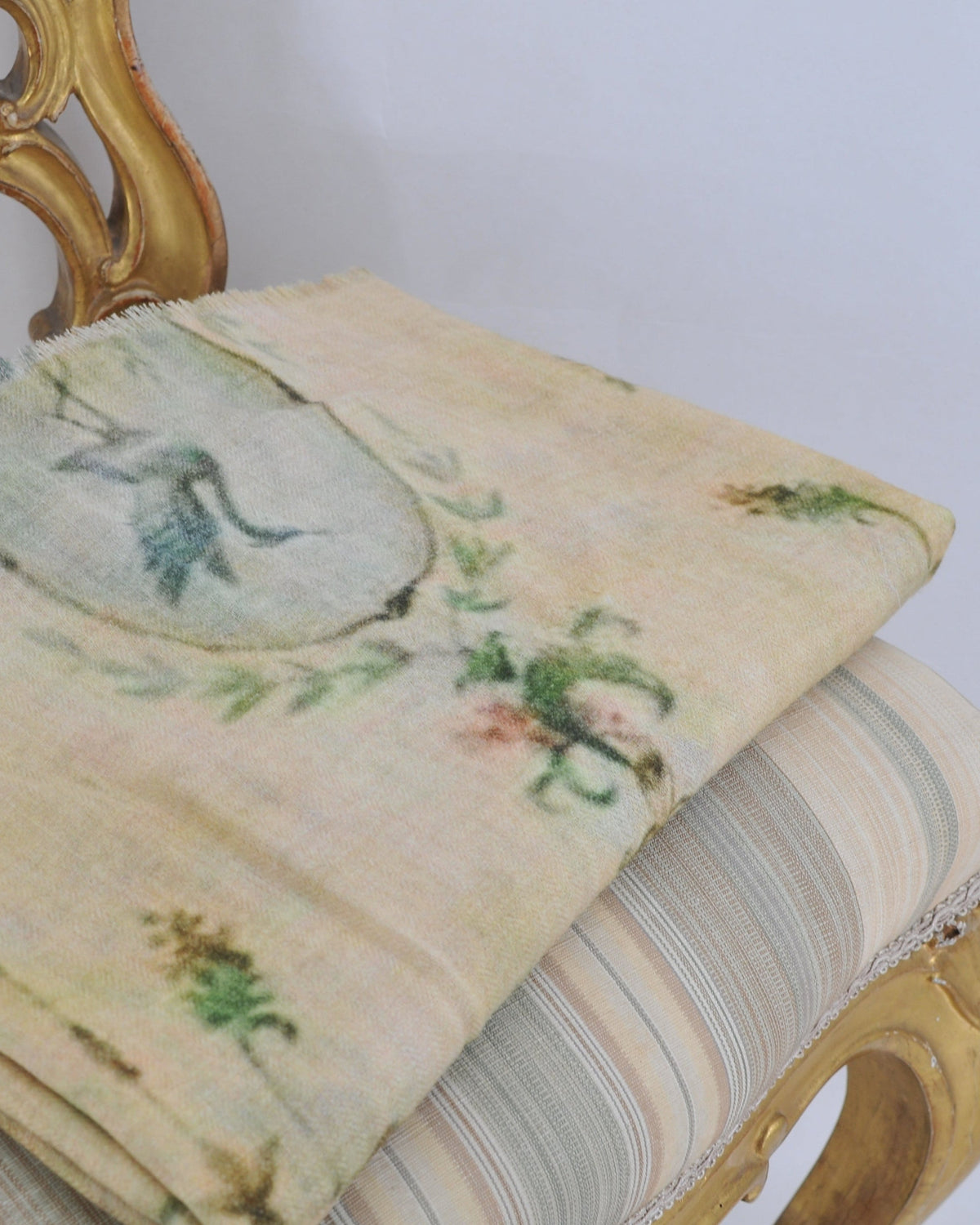 Folded cream Fiore shawl displaying delicate green botanical print on classic chair for women T.ba