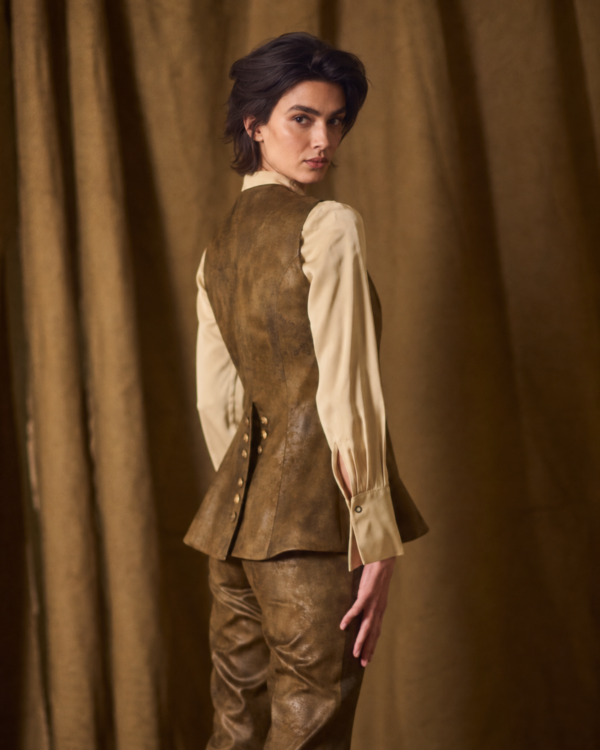 Three-quarter rear view of model showing the back tailored structure and metal buttons of the Gnu Baltea Vest in khaki suede for women by T.ba