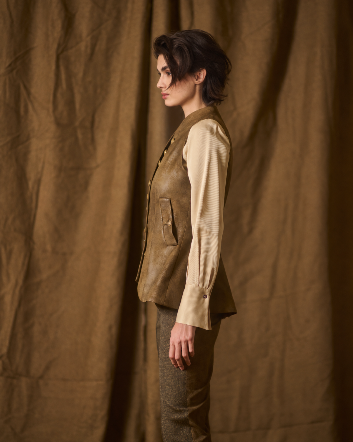 Side profile view of model wearing the Gnu Baltea Vest in khaki suede leather paired with a cream blouse for women by T.ba