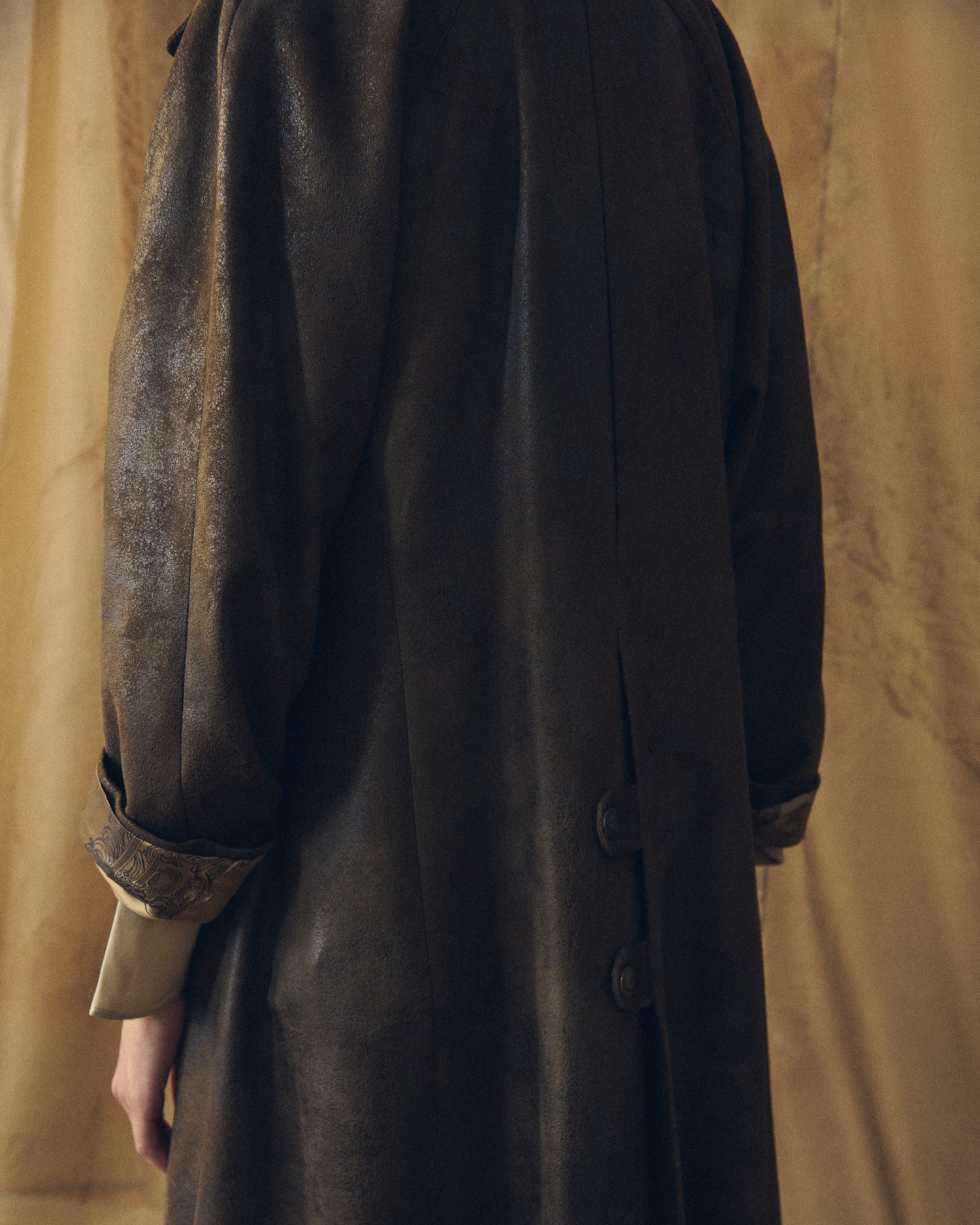 Back detail of the T.ba Gnu Biella coat in khaki waxed linen, focusing on the texture and the buttoned back tabs.
