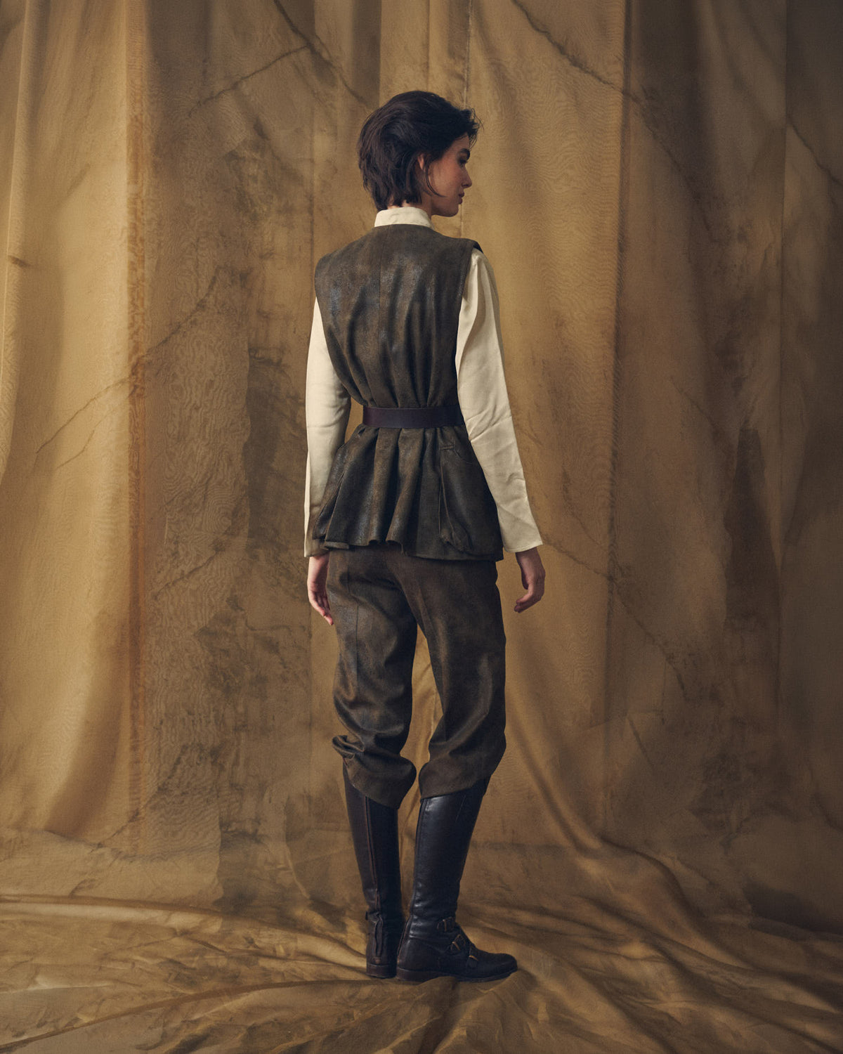 Back view of model wearing the belted khaki Gnu Shooting Vest showing the pleated peplum waist silhouette by T.ba
