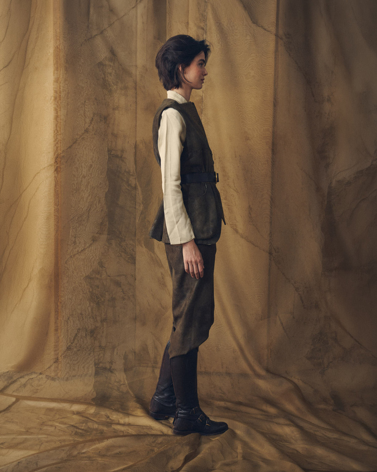 Side profile view of model wearing the khaki Gnu Shooting Vest paired with matching trousers and riding boots by T.ba