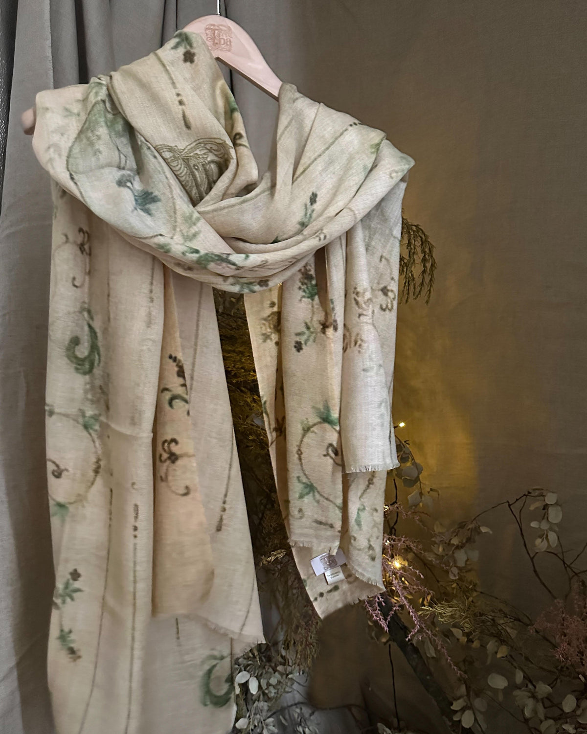 Fiore fine wool shawl in beige featuring green botanical print hanging on hanger for women T.ba