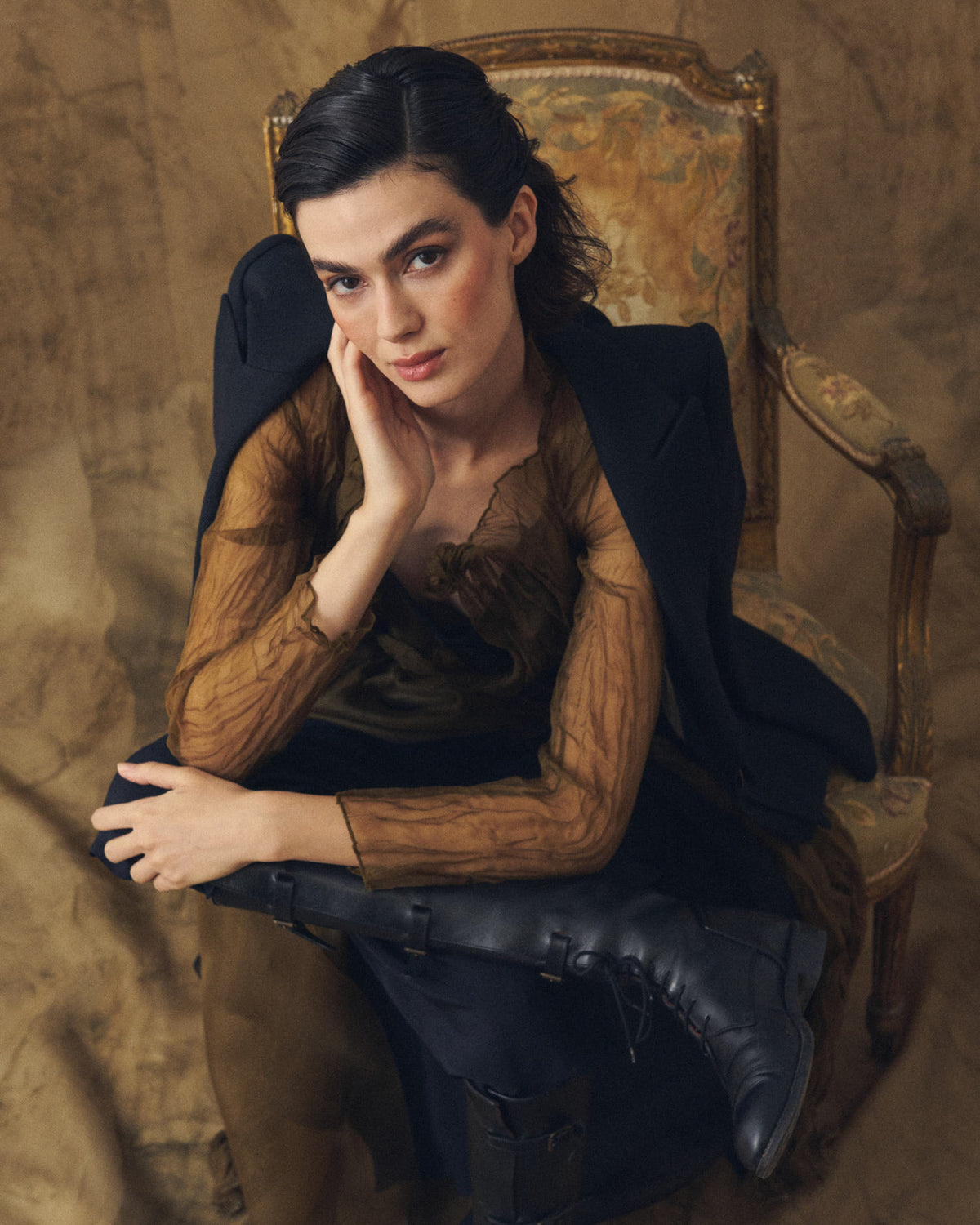 High angle shot of model sitting on vintage chair highlighting black leather straps knee-high boots T.ba