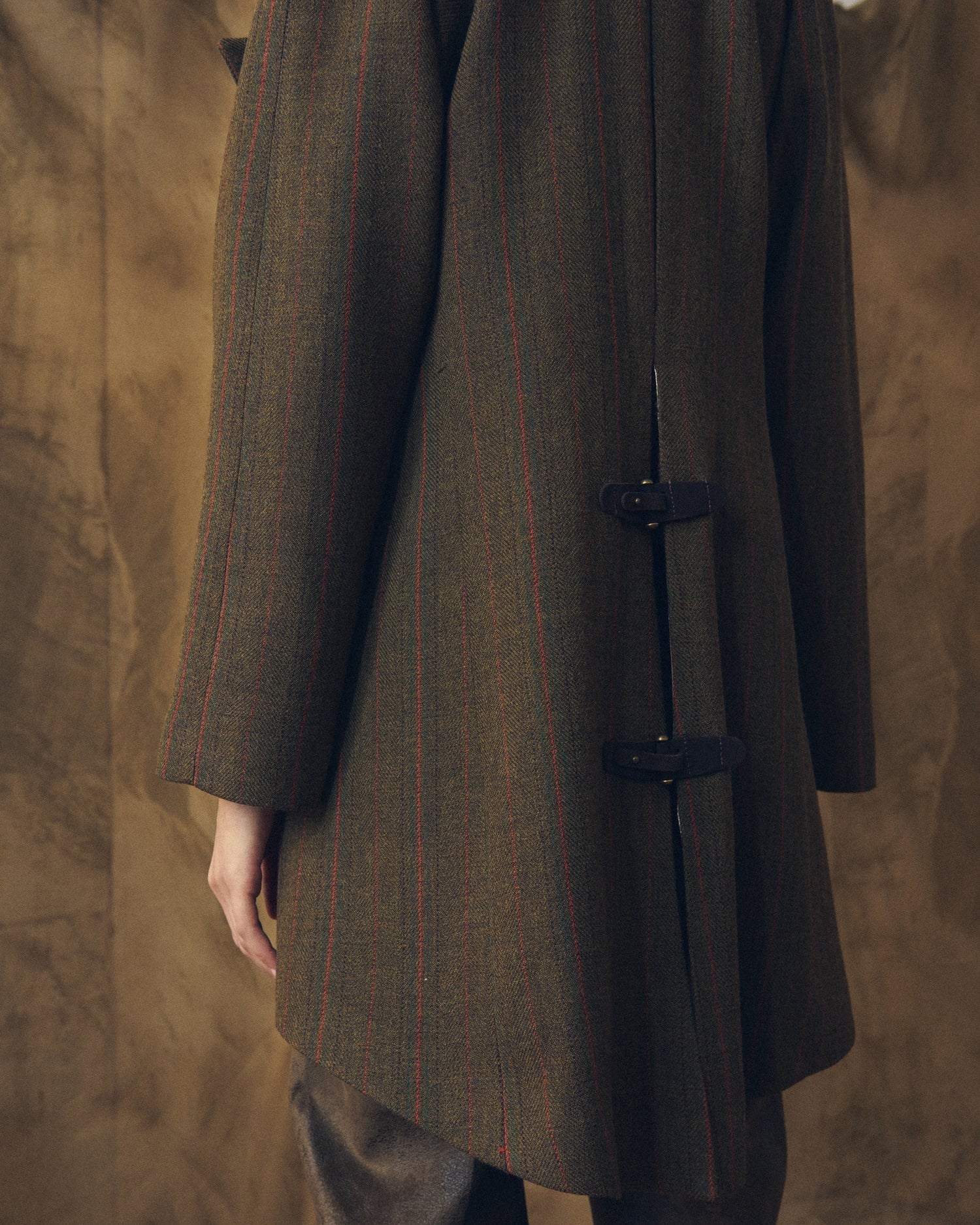 Close-up rear view of the Jerez Biella Field Coat in khaki wool tweed highlighting the back vent and leather buckle closures by T.ba.
