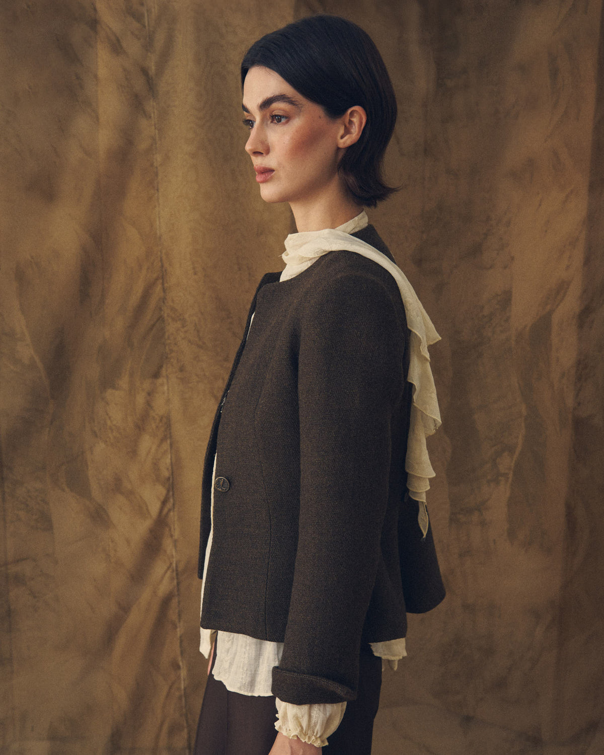 Side profile view of model wearing the collarless Jerez Greta cropped jacket in dark brown wool by T.ba