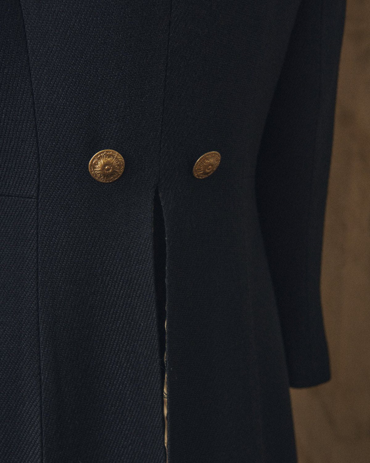 Close-up shot highlighting the fine twill wool texture and antique gold decorative buttons on the back of the Jerez Lancelot Combi Coat for women by T.ba
