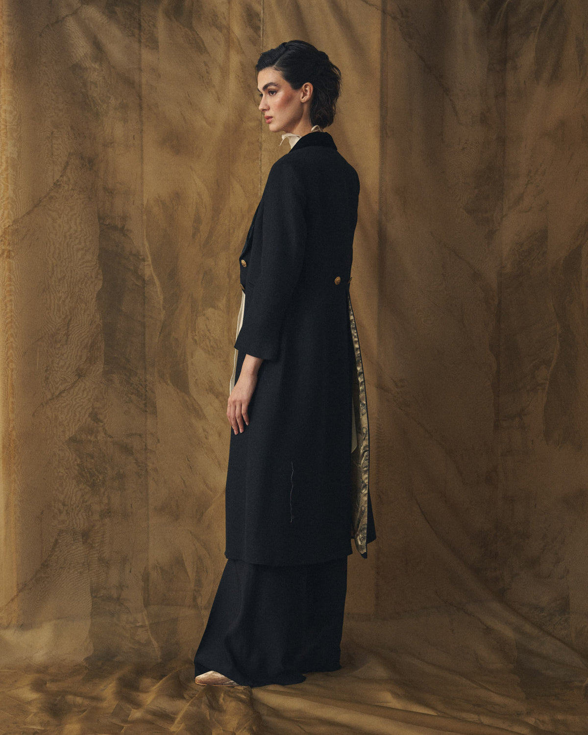 Side profile view of model featuring the tailored silhouette and patterned lining of the Jerez Lancelot Combi Coat in black for women by T.ba