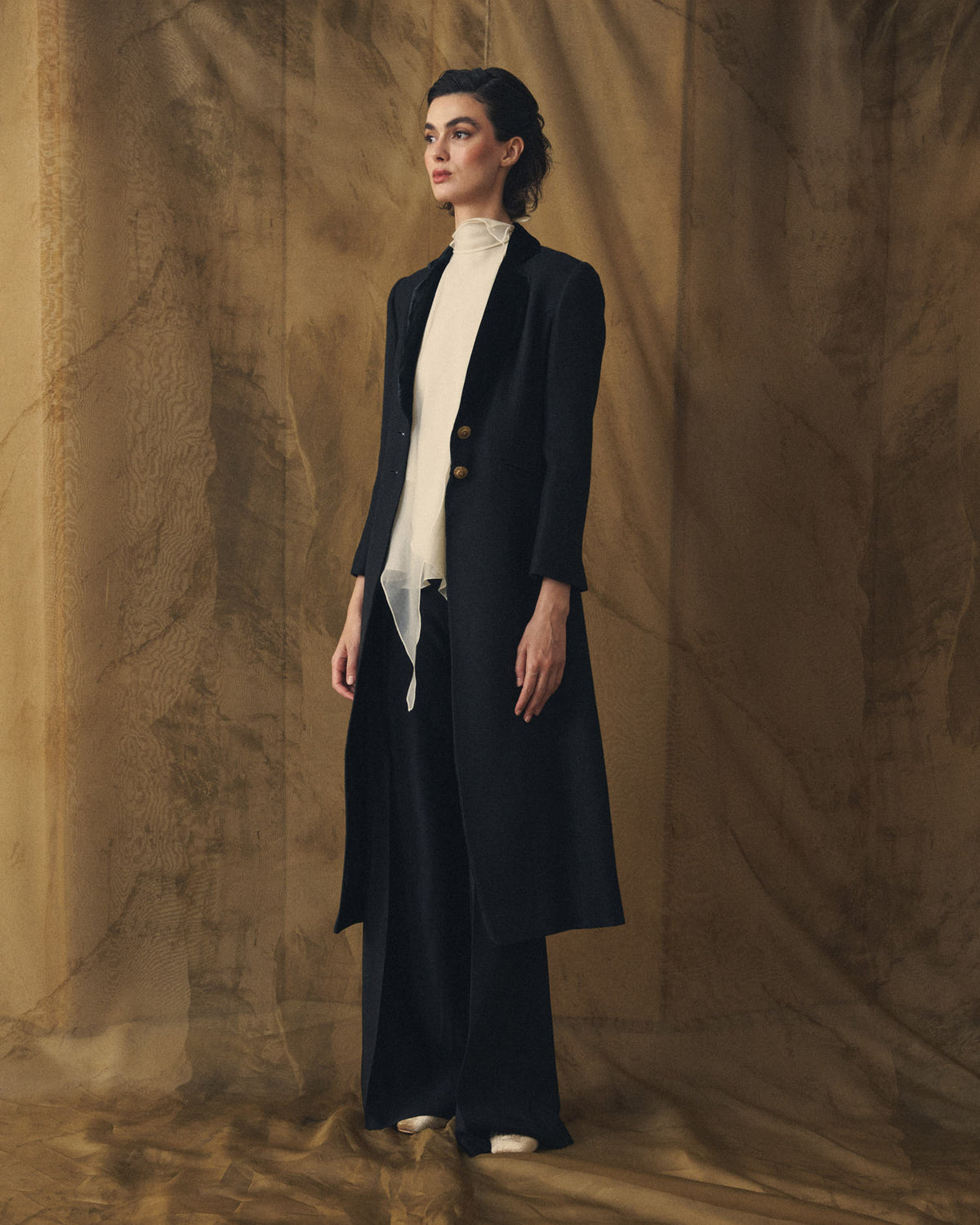 Three-quarter view of model showcasing the Jerez Lancelot Combi Coat black long frock coat with velvet lapels for women by T.ba