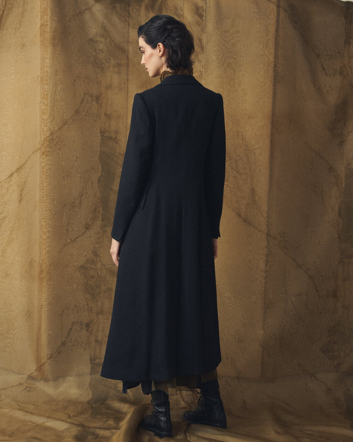 Three-quarter back view of model showcasing the tailored silhouette and back drape of the Jerez Verdi Coat in black wool for women by T.ba