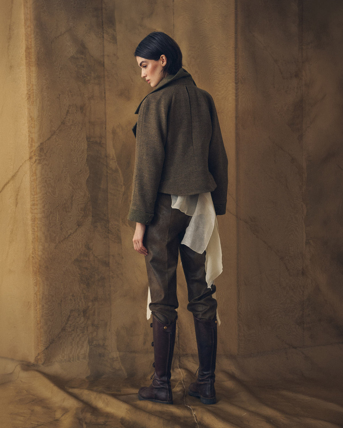 Back view of model wearing dark brown leather straps knee-high boots paired with riding trousers T.ba