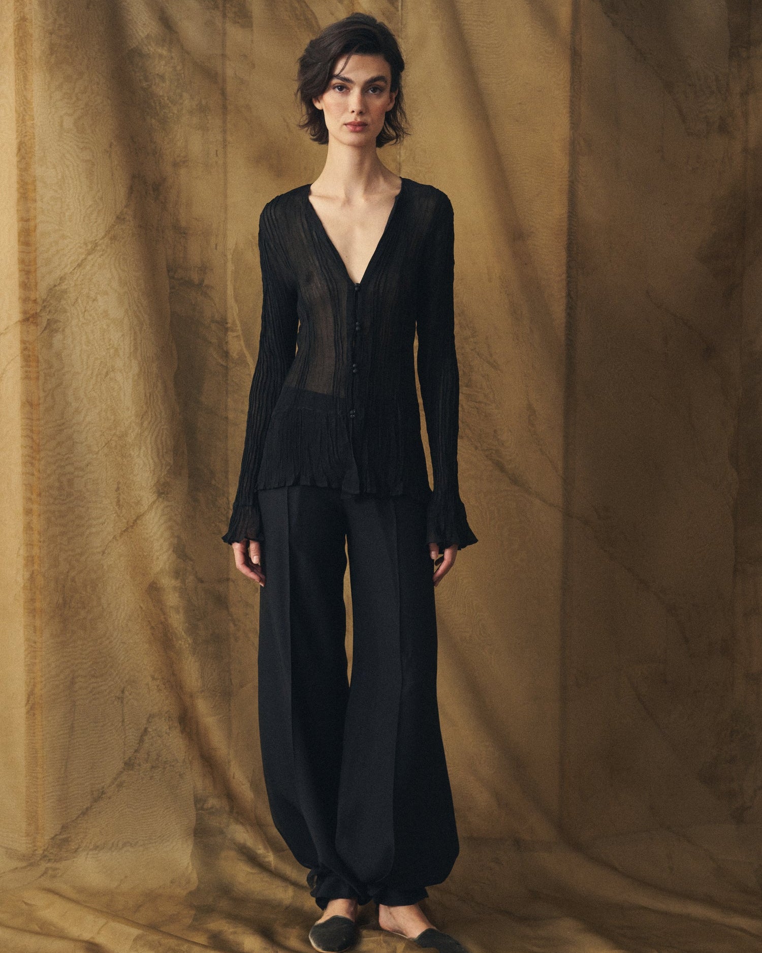 Full-length front view of the Lizzie pleated black chiffon blouse with V-neck styled with fluid trousers for women T.ba