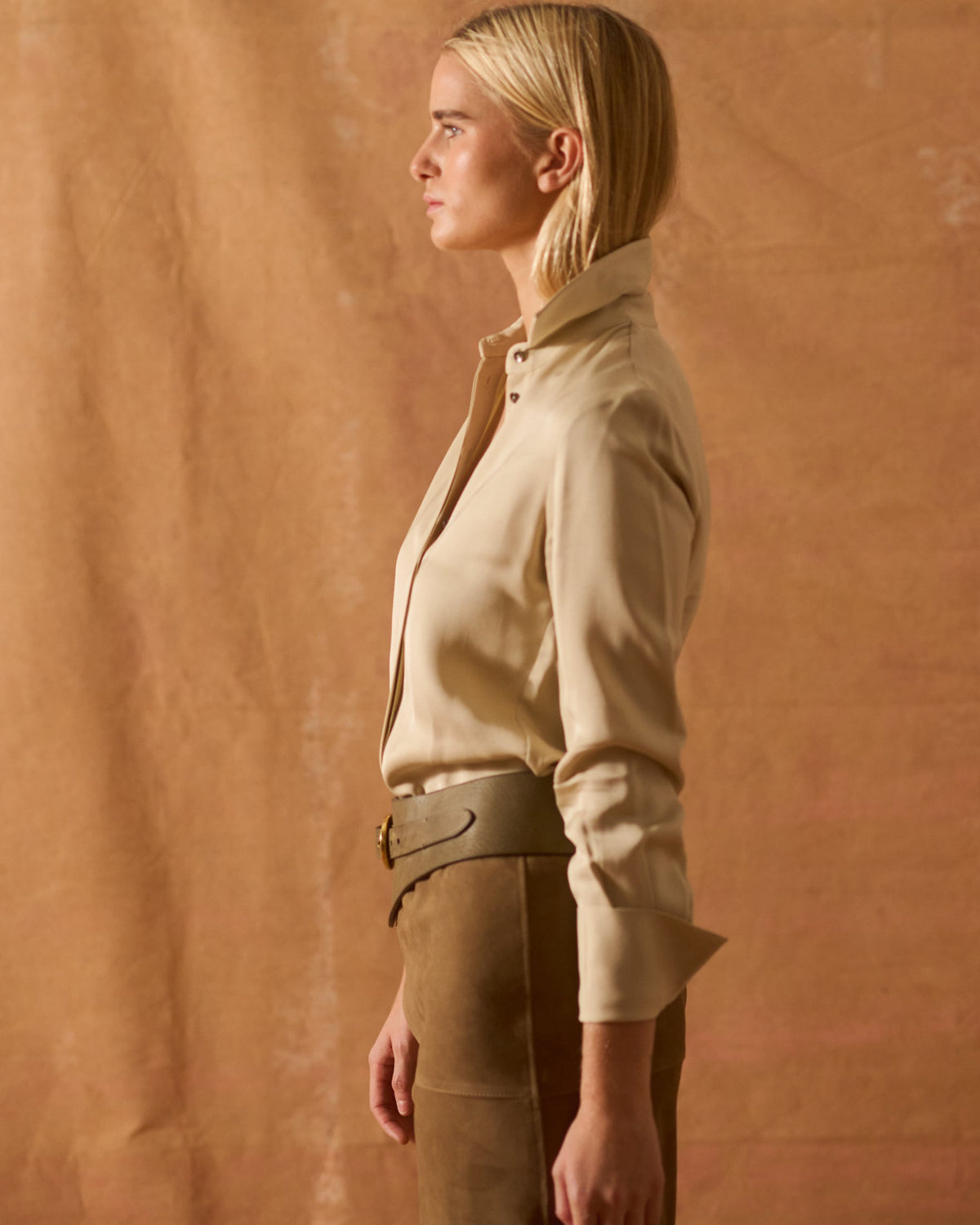 Side view of model showing tailored silhouette and cuffed sleeves of beige Rania silk shirt T.ba