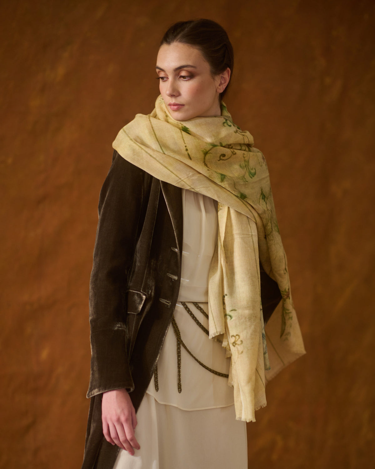 Medium shot of woman wearing cream Fiore shawl with subtle green floral pattern and fringed edge T.ba