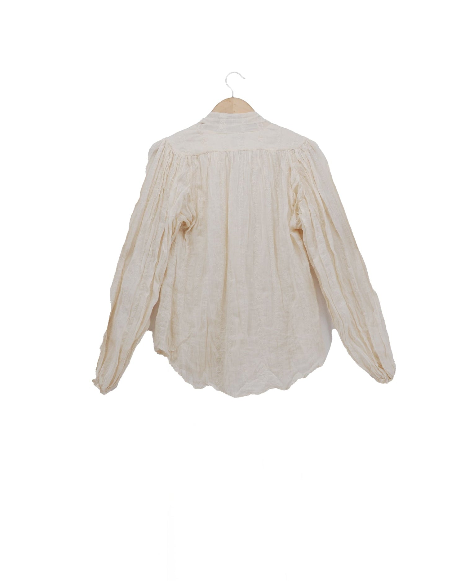 Back side of women's embroidered natural off-white ramie Pienza blouse featuring raw-edge cascade ruffles, neck tie detail, and pleated long sleeves by T.ba