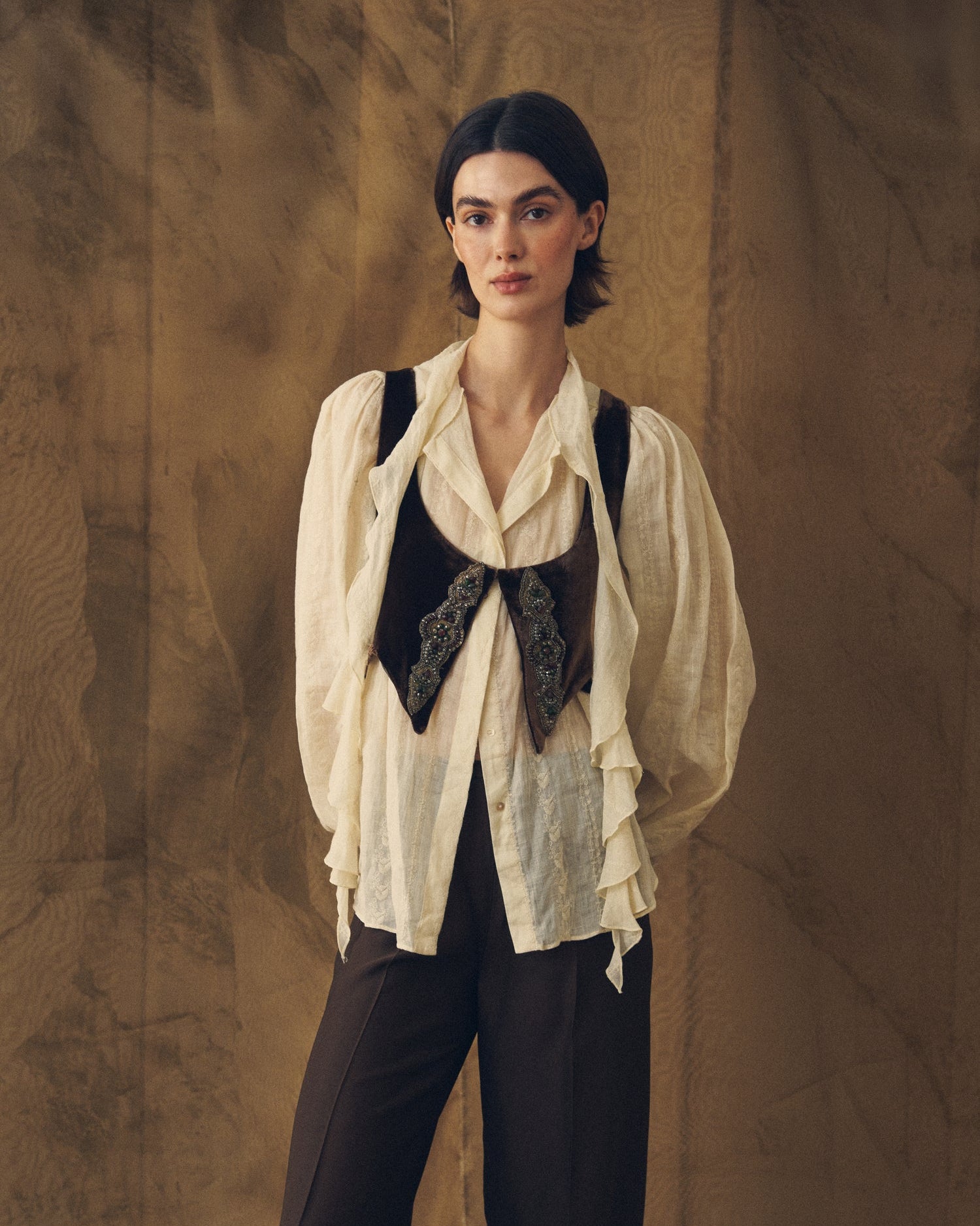 Medium shot of model wearing the Ramie Embroidered Pienza Blouse in natural sheer fabric with ruffles for women by T.ba