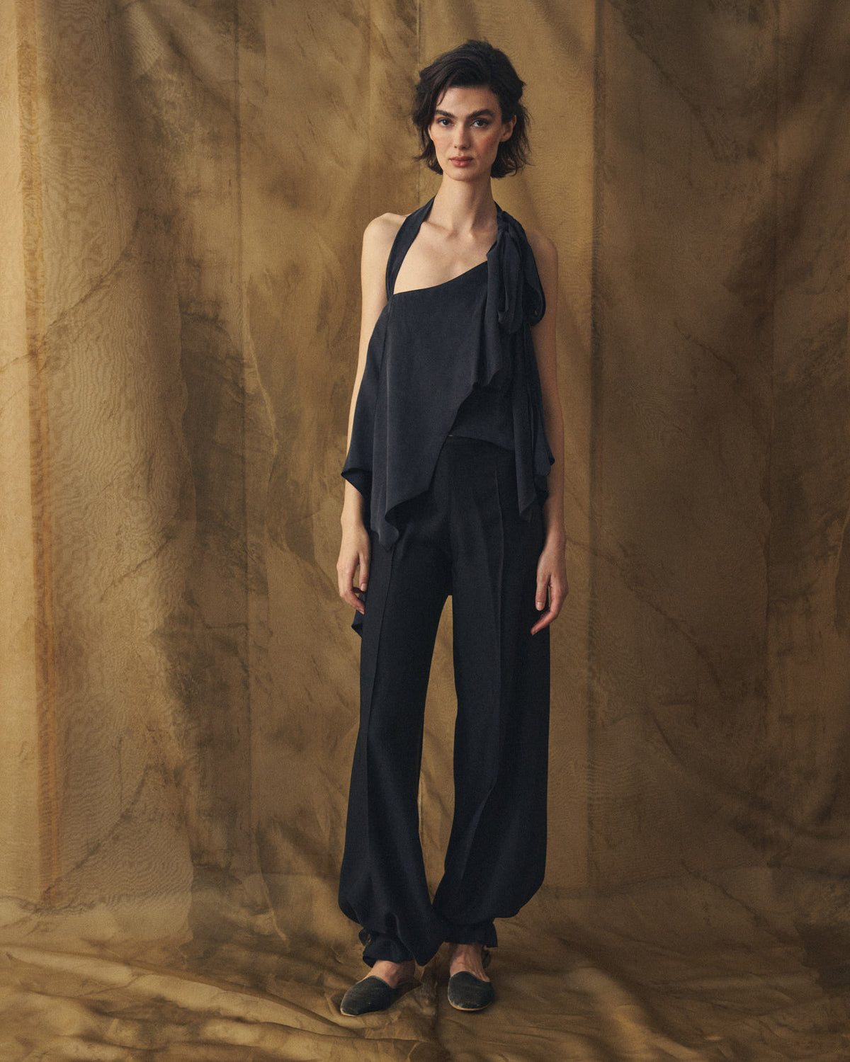 Full-length front studio shot of model wearing the black Sam cupro halter neck top with matching fluid trousers by T.ba
