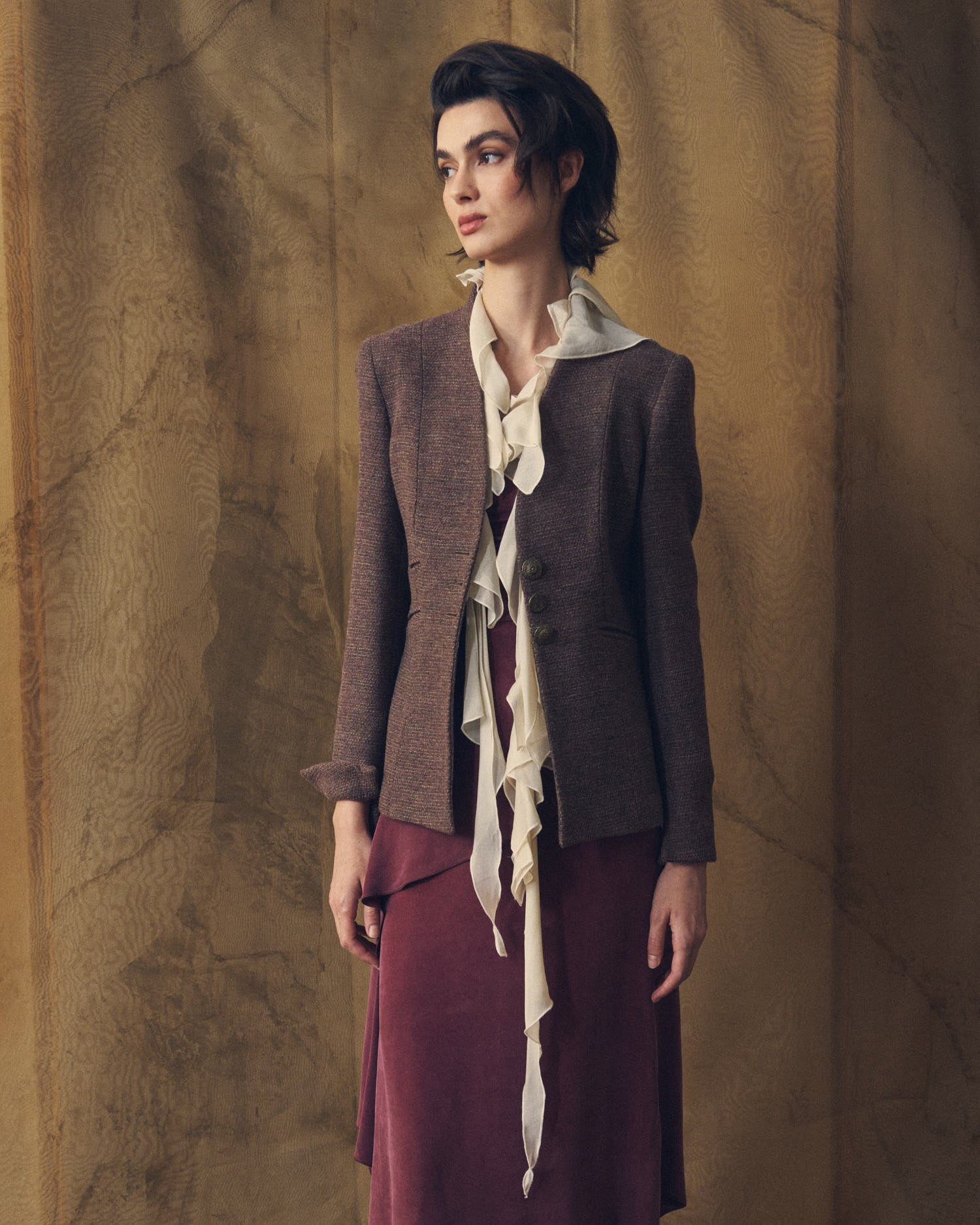 Three-quarter front view of model wearing the brown Sam tweed jacket styled over a ruffled blouse by T.ba