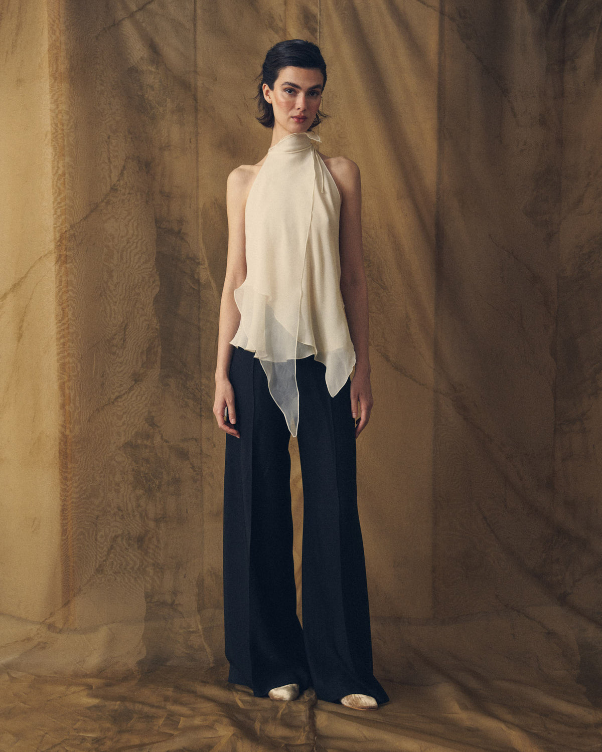 Full front view of model wearing the wide-leg Sharkskin Maxi Pants in black styled with an off-white silk halter top for women by T.ba