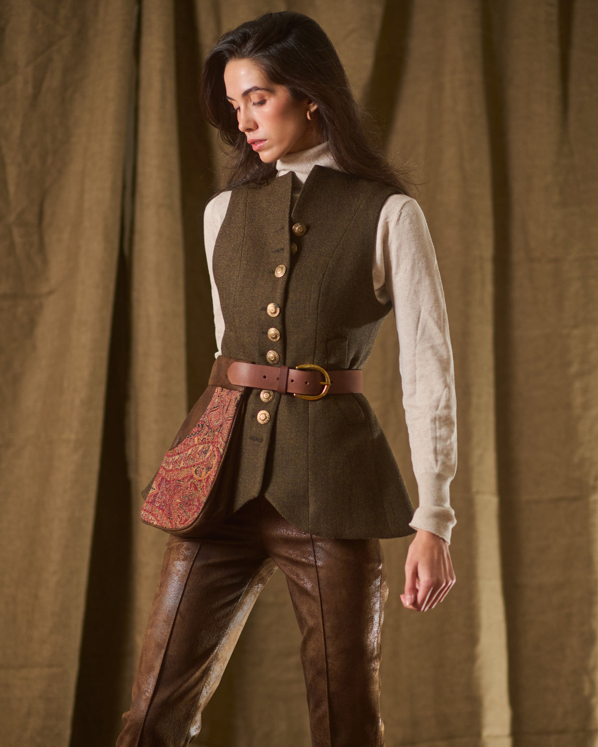 Side angle view of model wearing brown leather Duke belt pouch with paisley pattern styled over tweed vest T.ba
