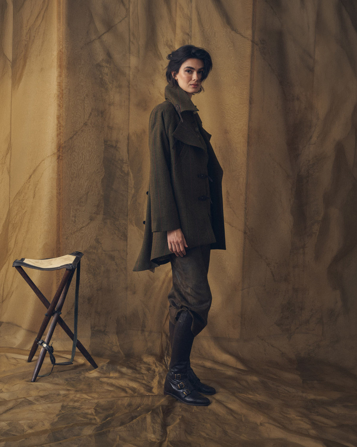 Side profile of model wearing high black leather boots with buckle accents and wool outerwear T.ba