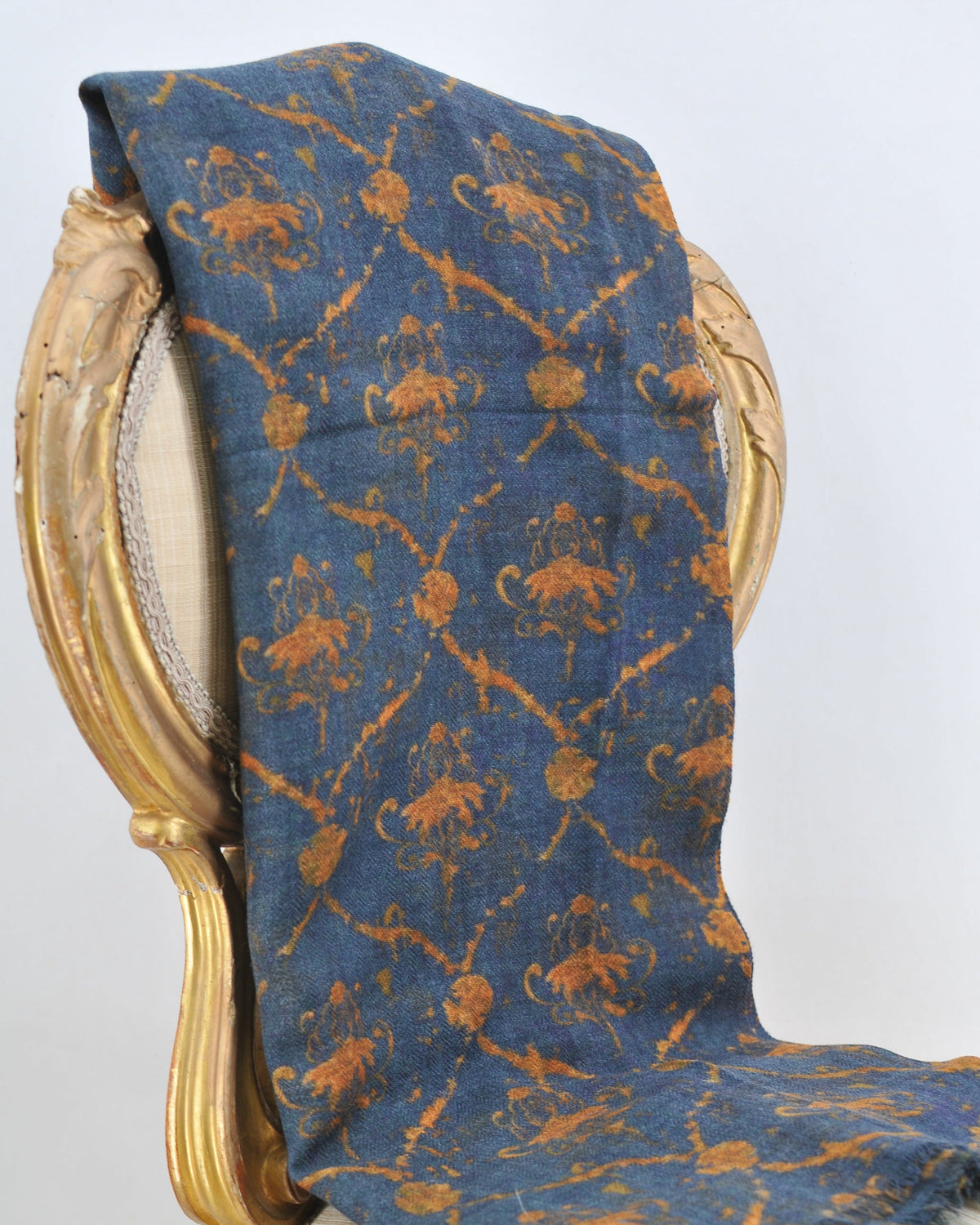 Studio shot of Versailles wool shawl draped over vintage chair showing blue wool with ochre damask motif for women T.ba